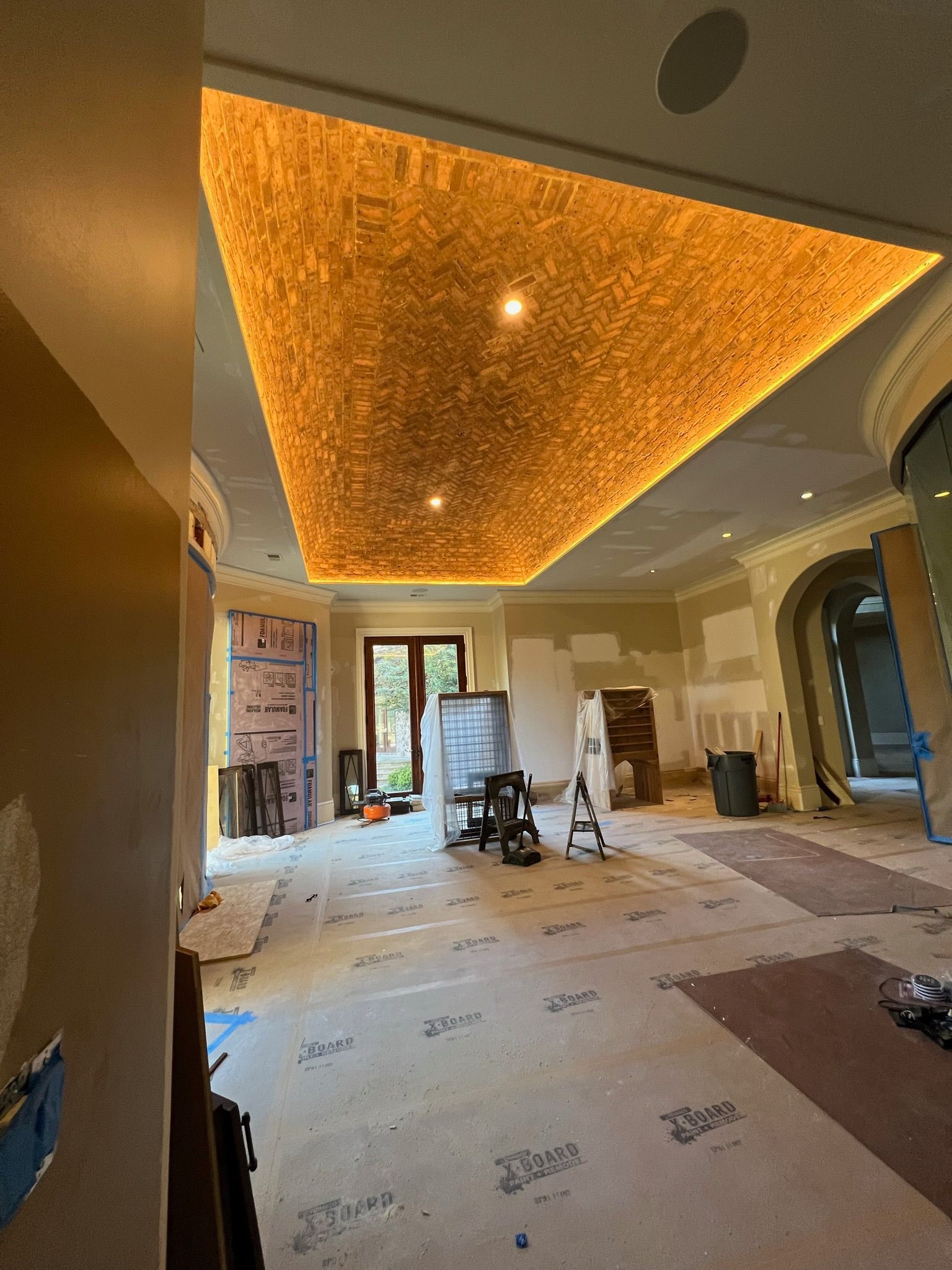 Room under construction with textured gold ceiling, two lights, open door and various building materials.