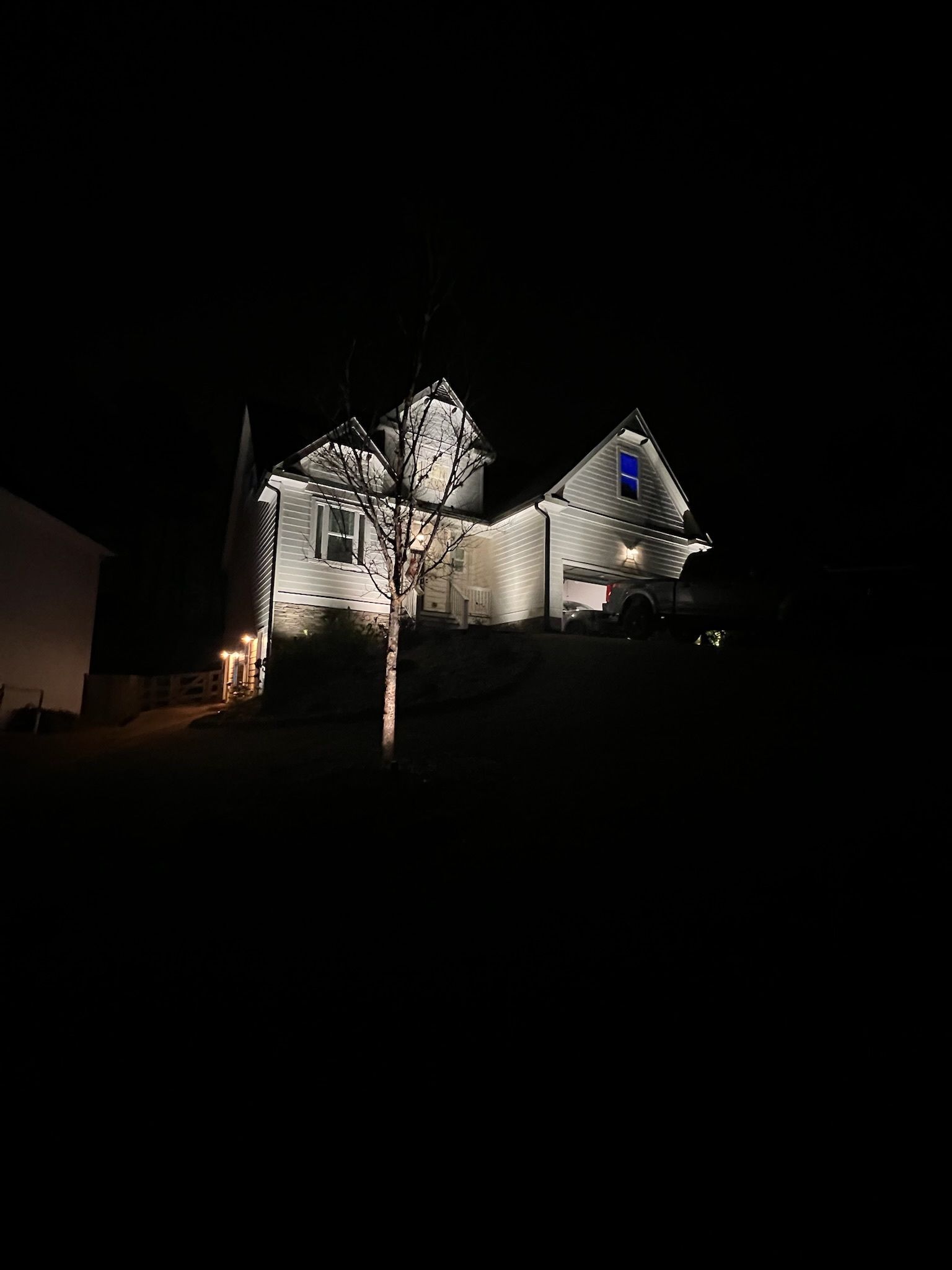 House at night, illuminated with white lights. Tree in front. Dark setting.