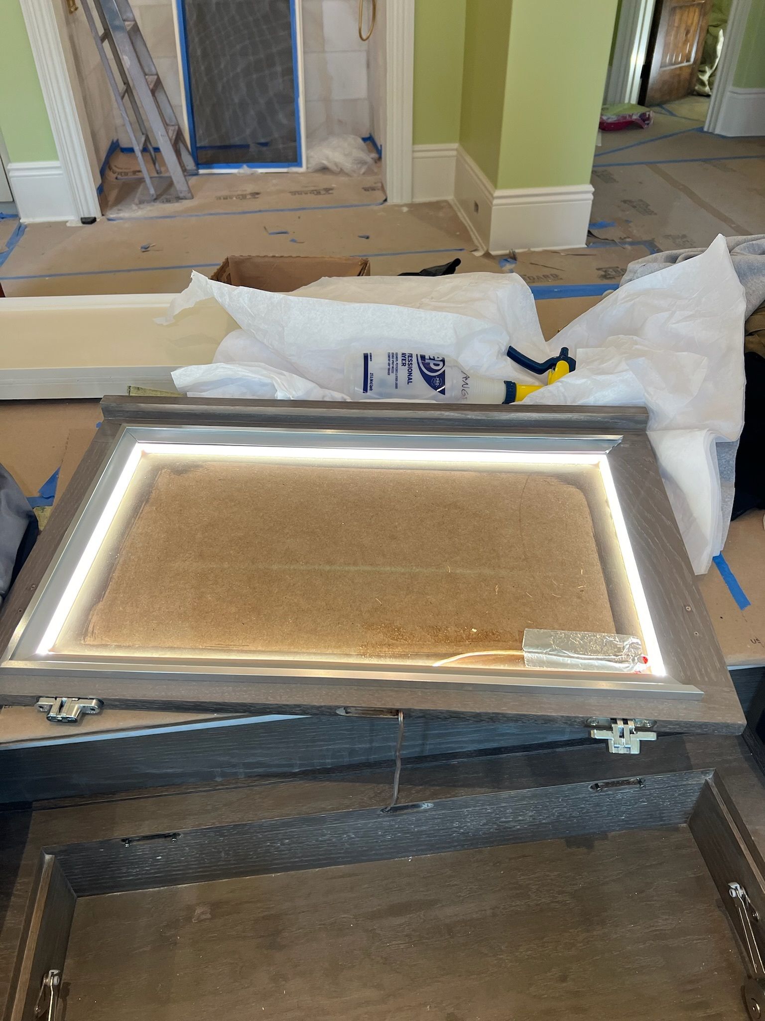 A framed mirror with built-in LED lighting, resting on cardboard. Construction site background.