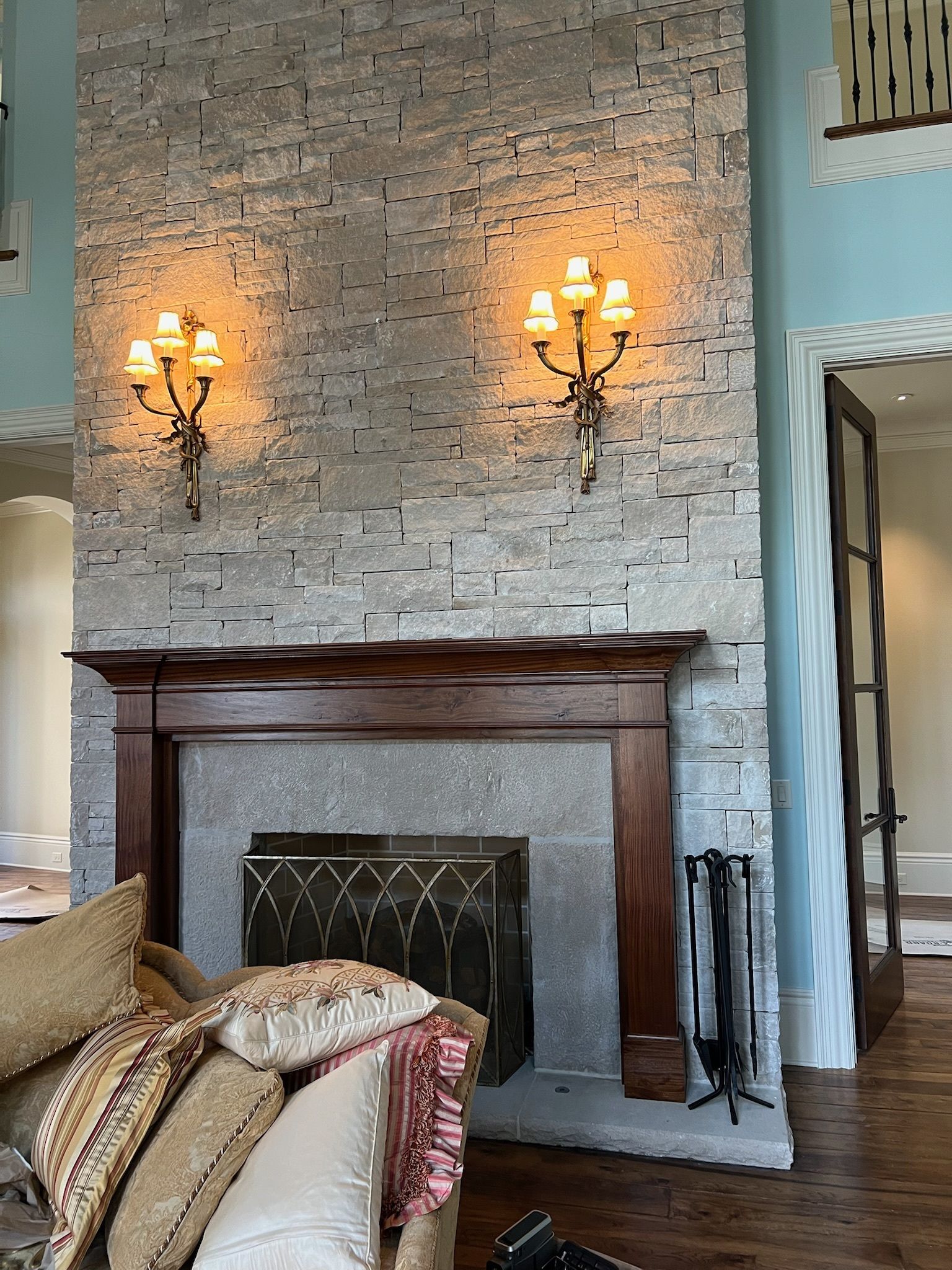 Fireplace with stone tile surround, sconces, wood mantel, and couch with pillows. Doorway on right.