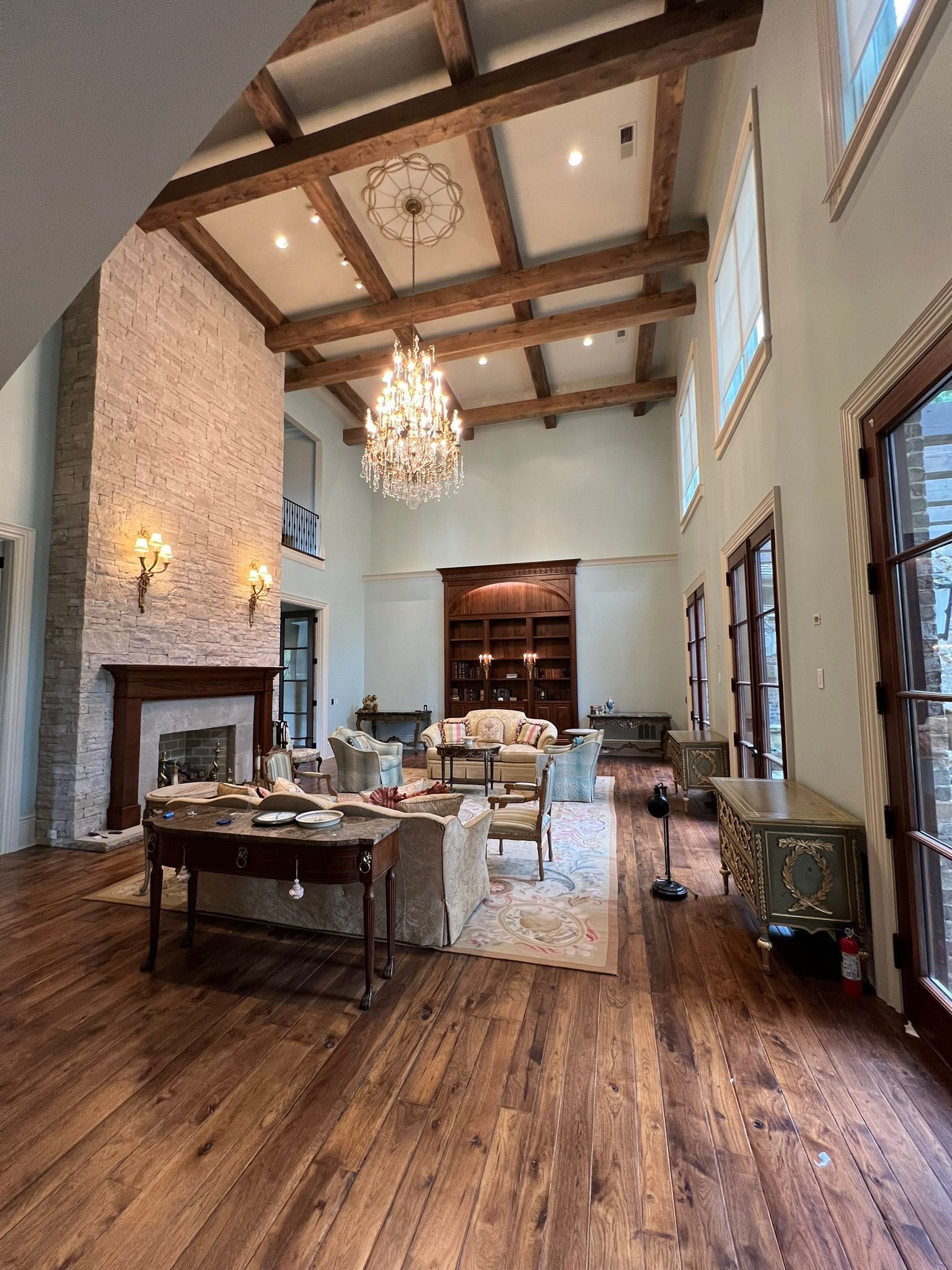 Large room with high ceilings, fireplace, chandelier, wooden beams, and ornate furniture.
