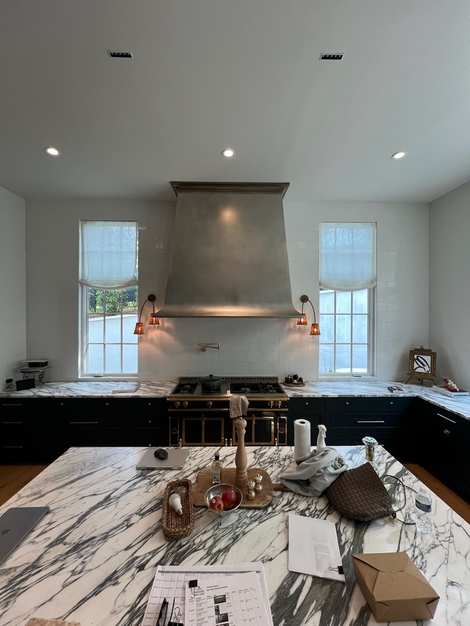 Kitchen with large marble island, dark cabinets, stainless steel range hood, windows.