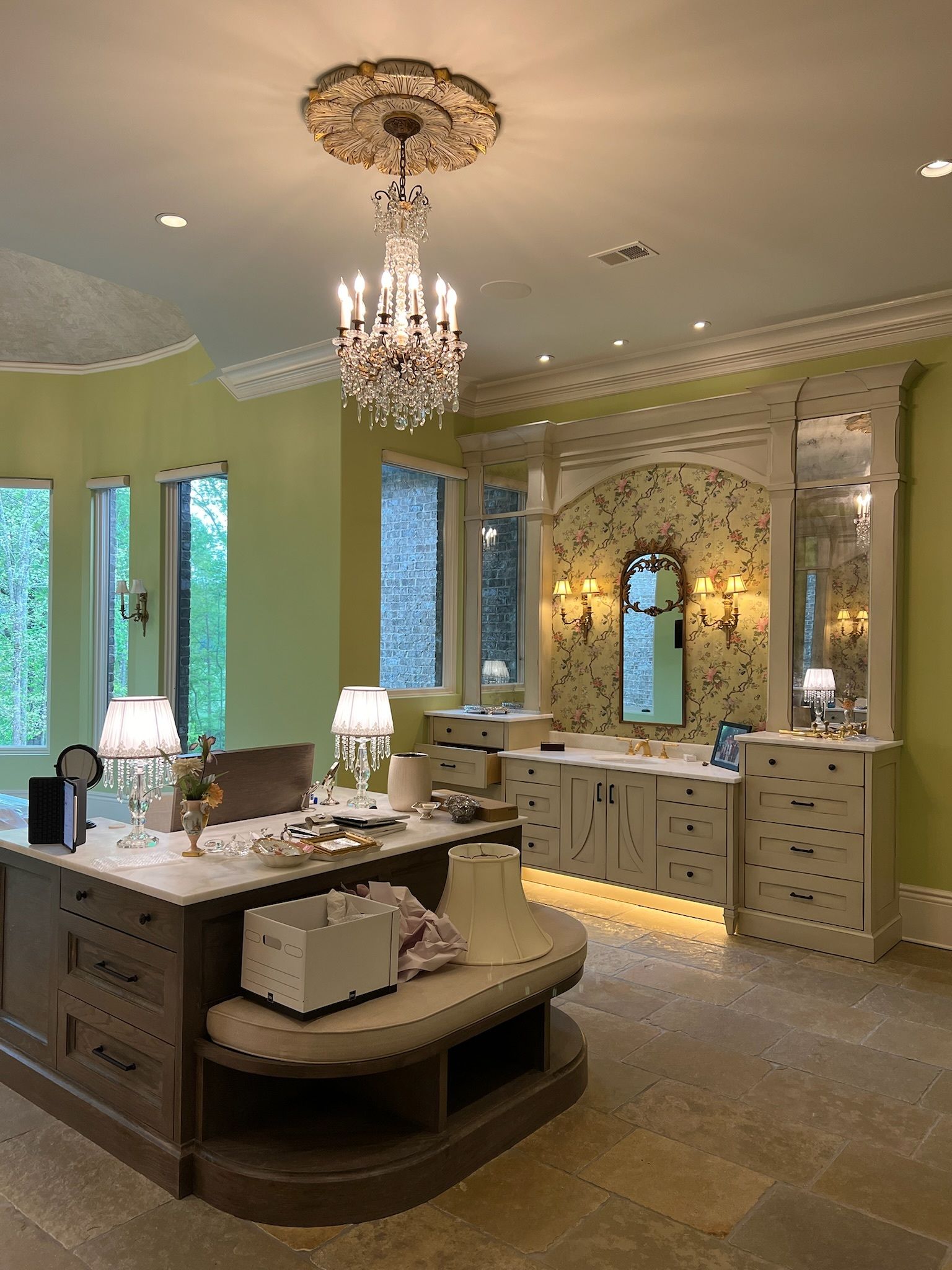 Luxurious bathroom with chandelier, vanity, and large countertop island, featuring a light green and cream color scheme.