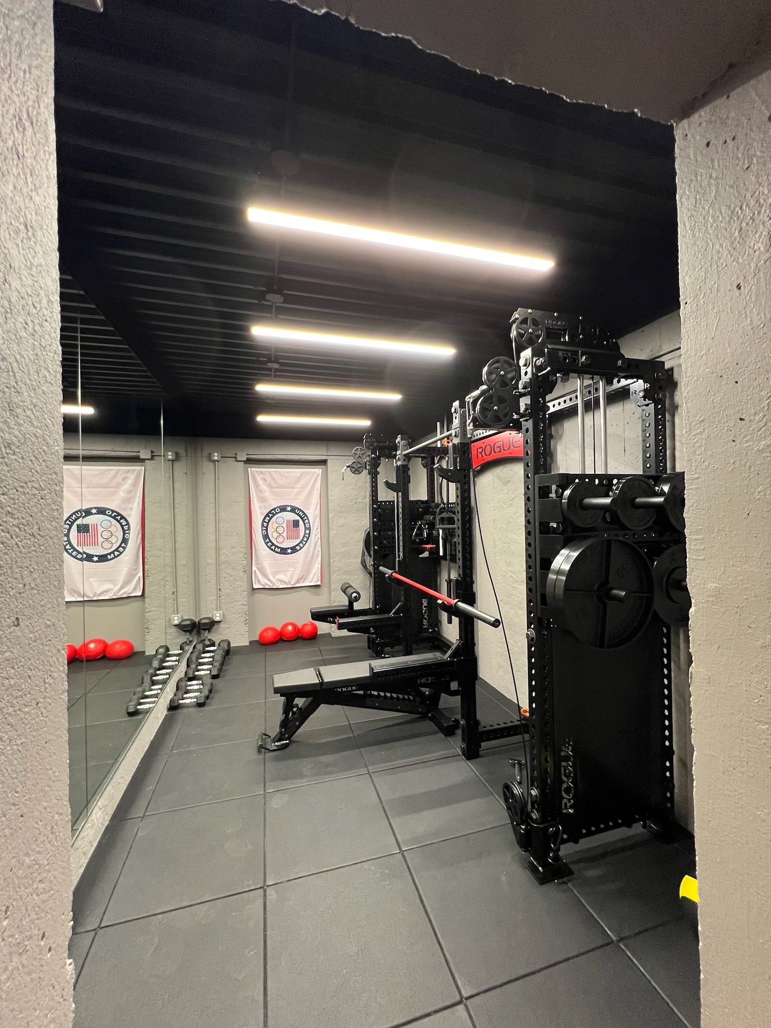 Gym interior with black equipment, weights, bench, flags, and rubber flooring.