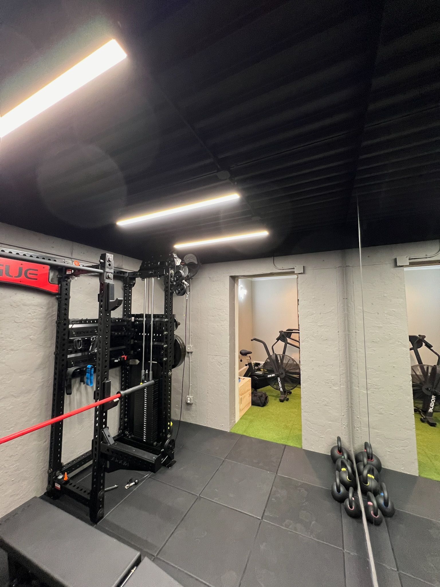 Weightlifting gym interior with black equipment, gray walls, and bright overhead lights.