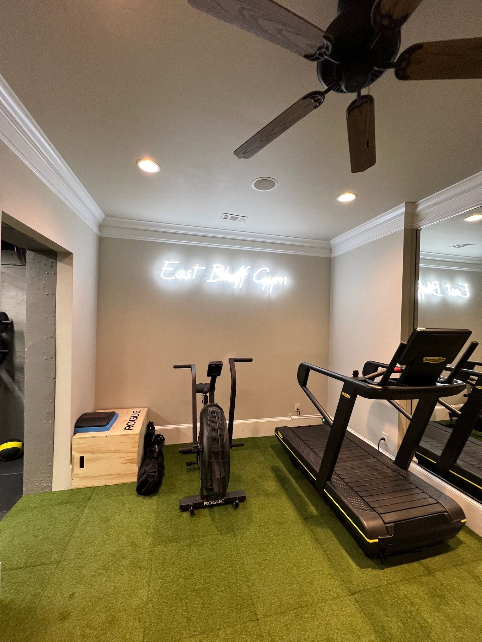 Home gym with workout equipment on green turf and neon sign: 