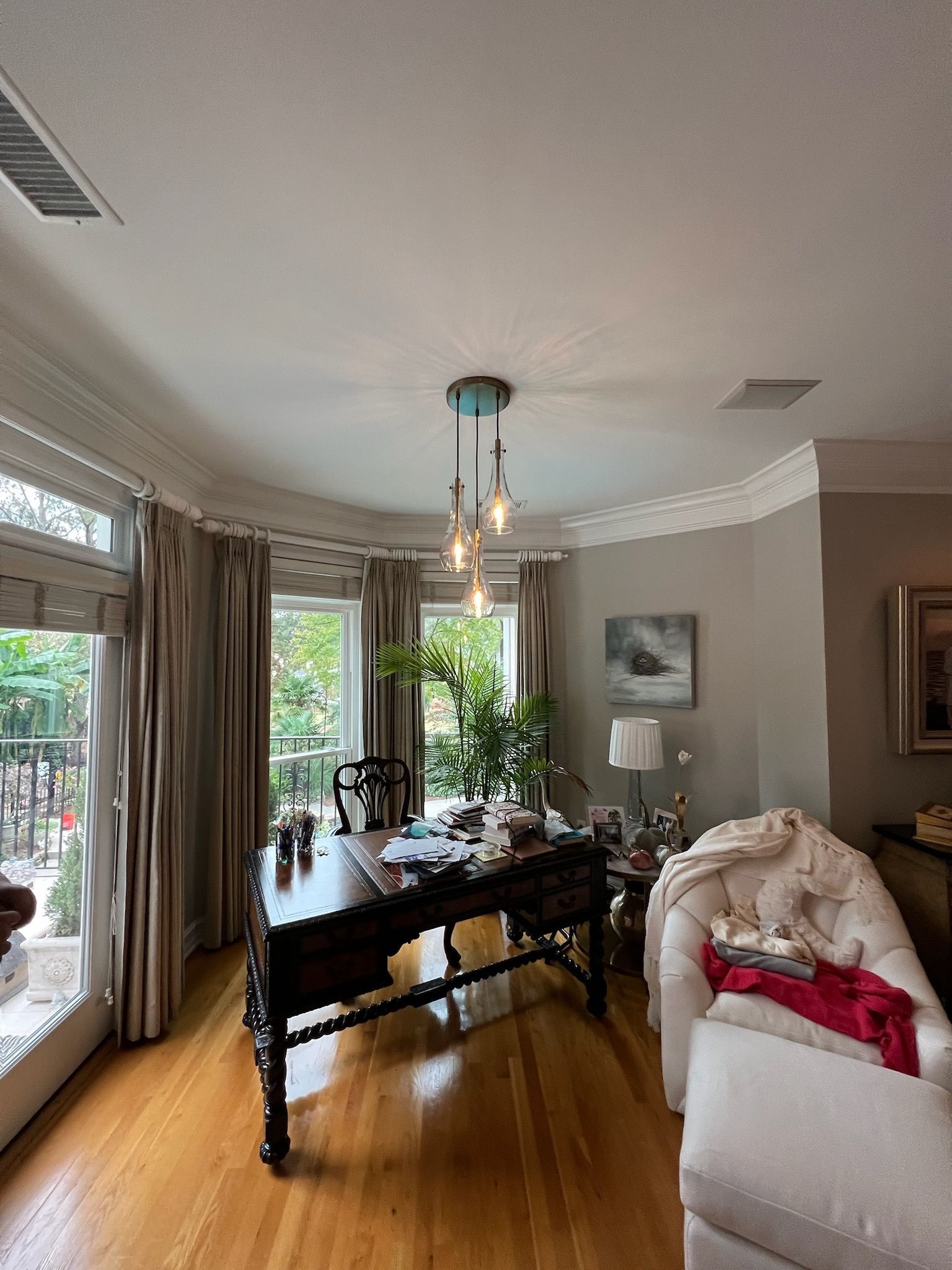A home office with a dark wooden desk, white sofa, and a three-light pendant.