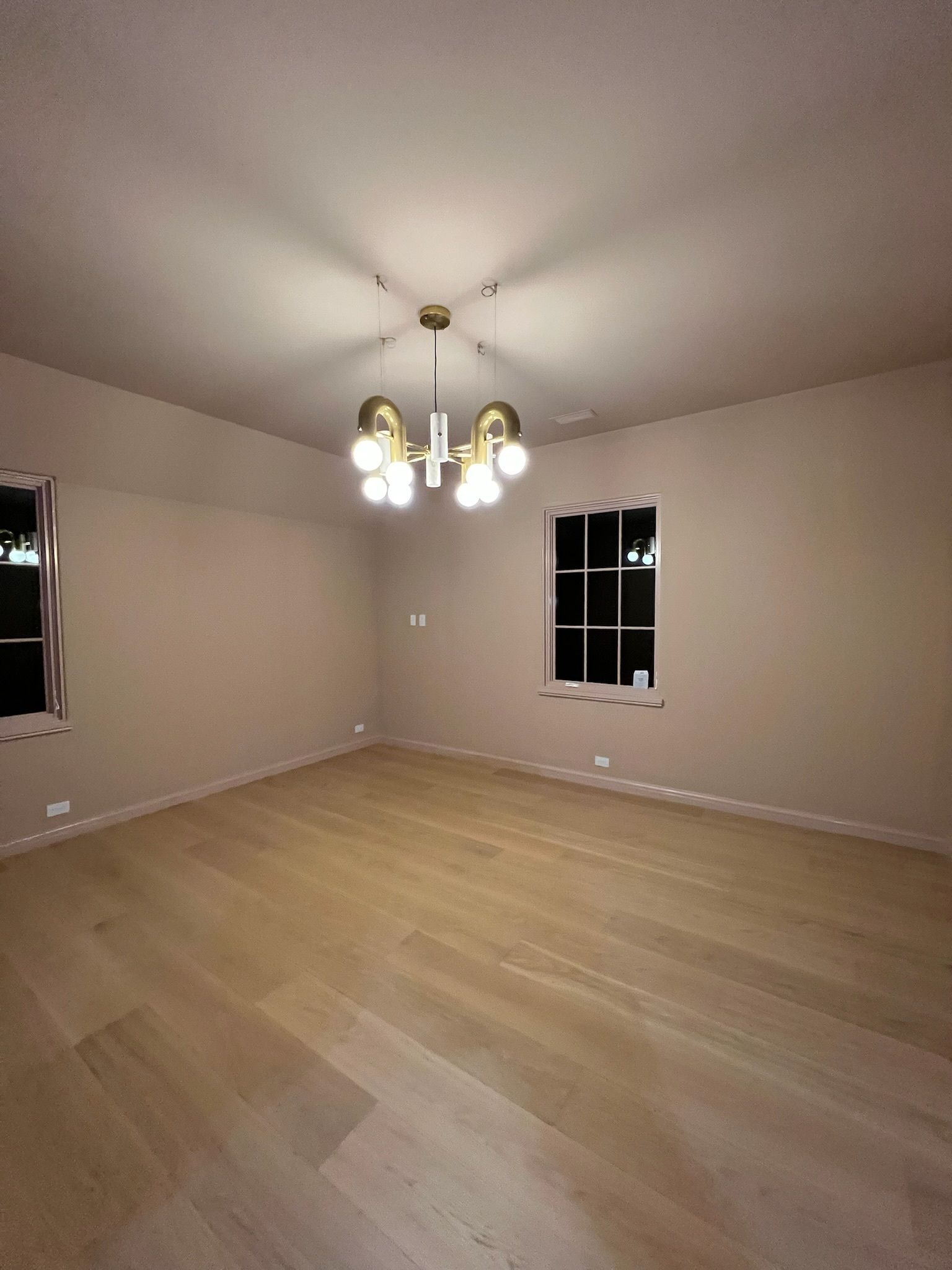 Empty room with light wood floors, beige walls, and a modern chandelier.
