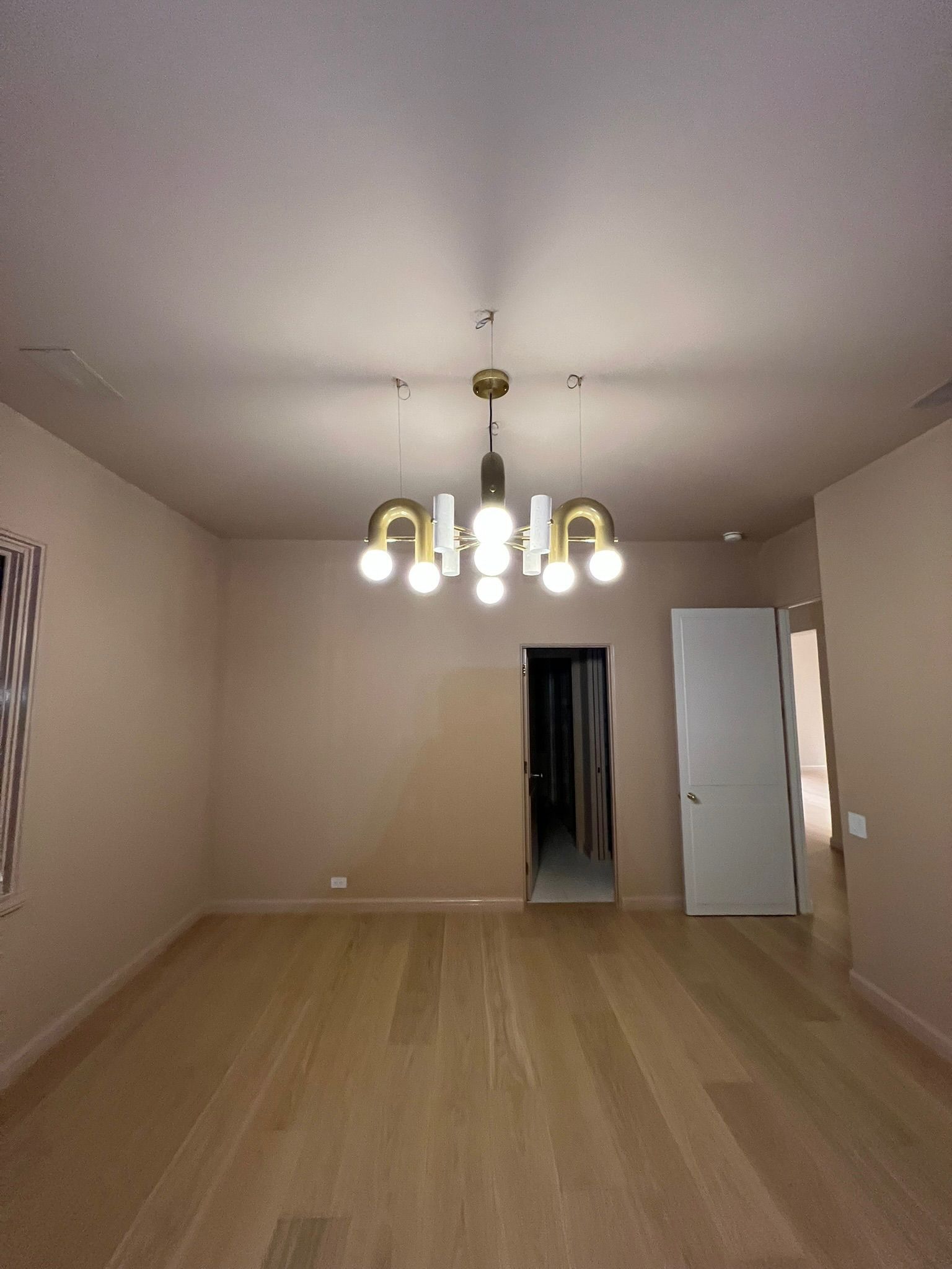 Empty room with light-colored walls and wood floors. A modern chandelier hangs from the ceiling.