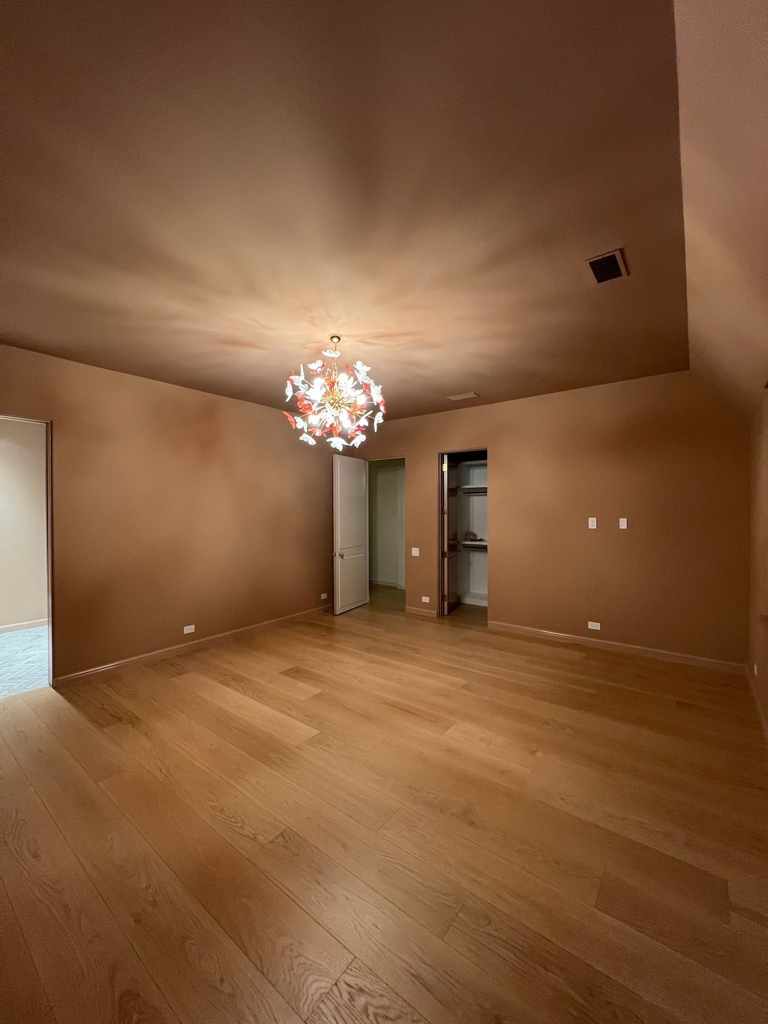 Empty room with hardwood floors, tan walls, and a decorative light fixture.