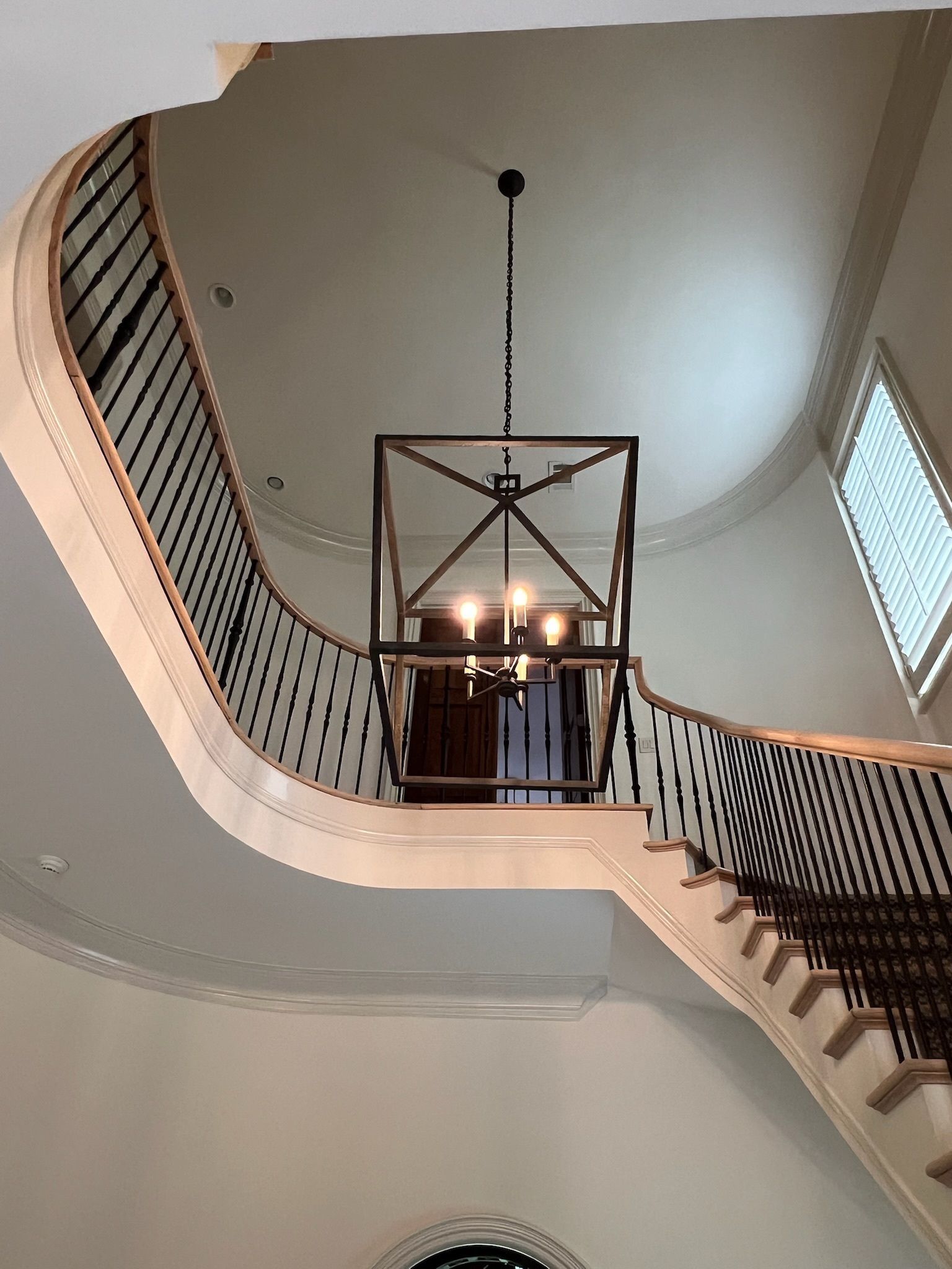 Grand staircase with a geometric chandelier, white walls, and dark metal railing.