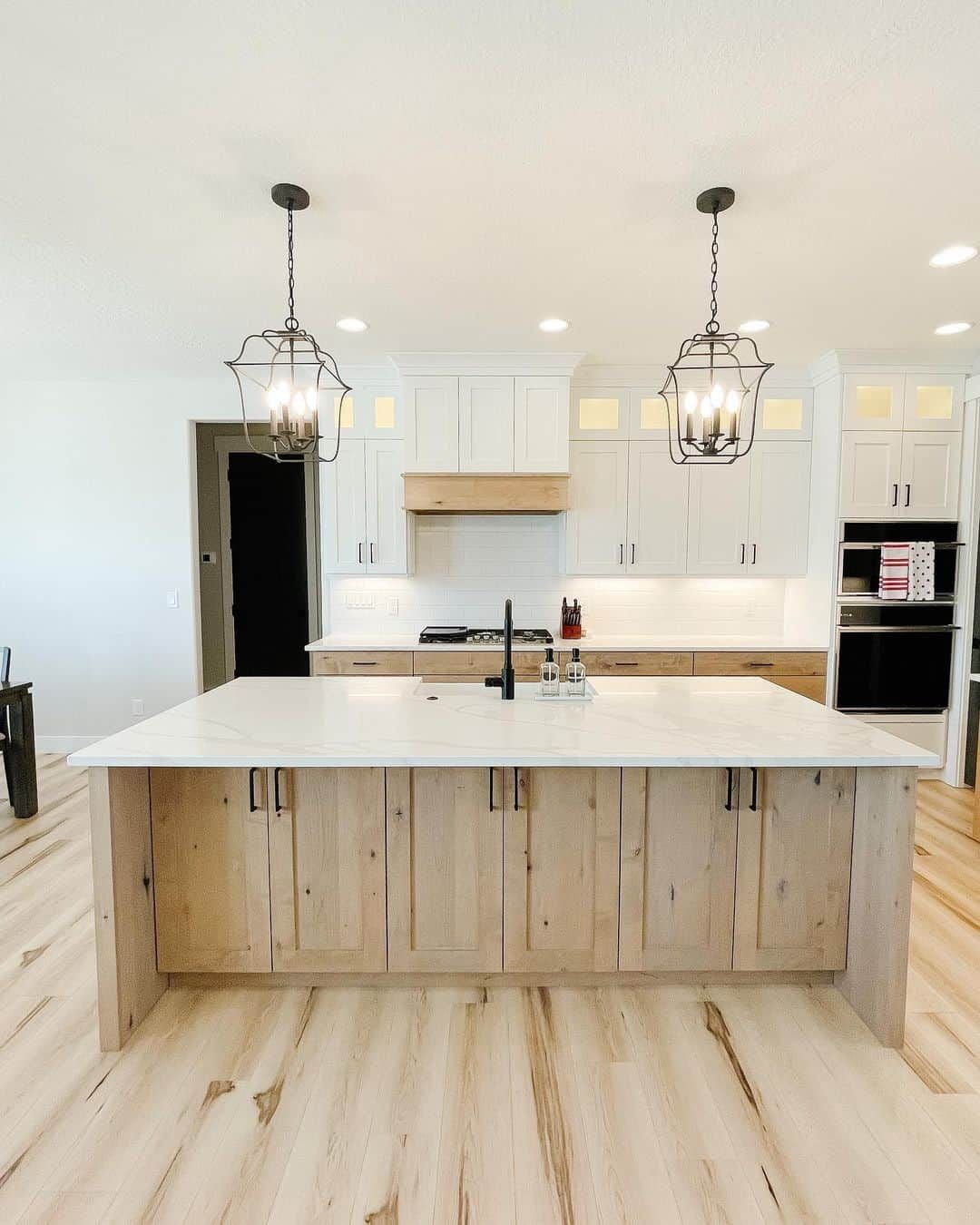 Kitchen with a light wood island and cabinets, white countertops, and black pendant lights.