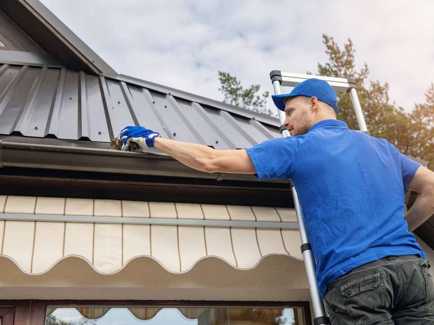 A man is standing on a ladder fixing a gutter on a roof.
