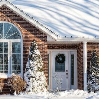 A brick house with a white door and a christmas tree in front of it covered in snow.