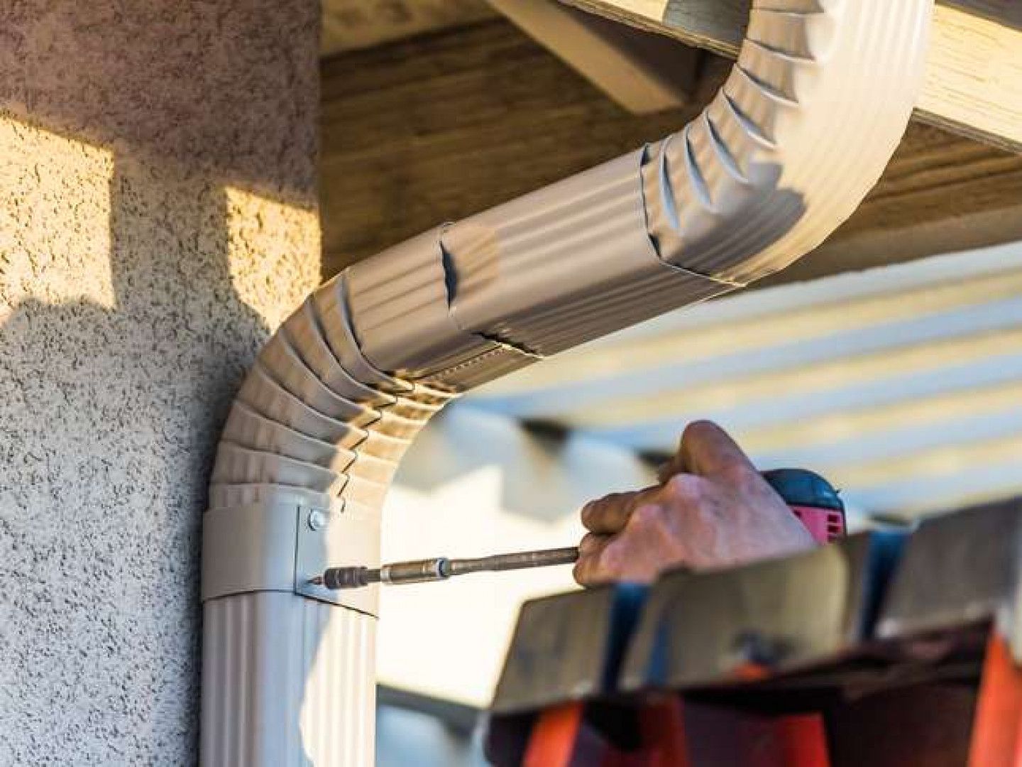 A man is fixing a gutter with a screwdriver.