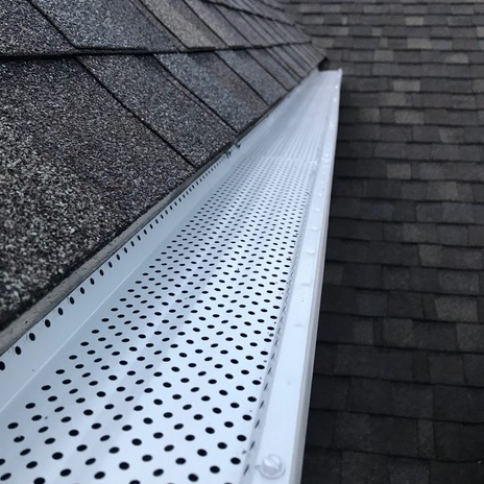 A white gutter with holes in it is on a roof.