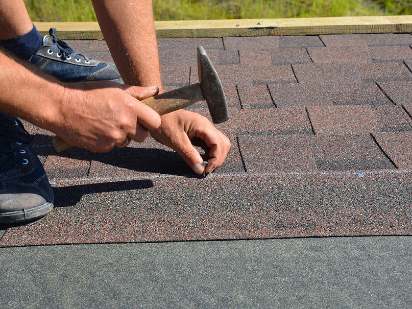 A man is hammering nails into a roof with a hammer.