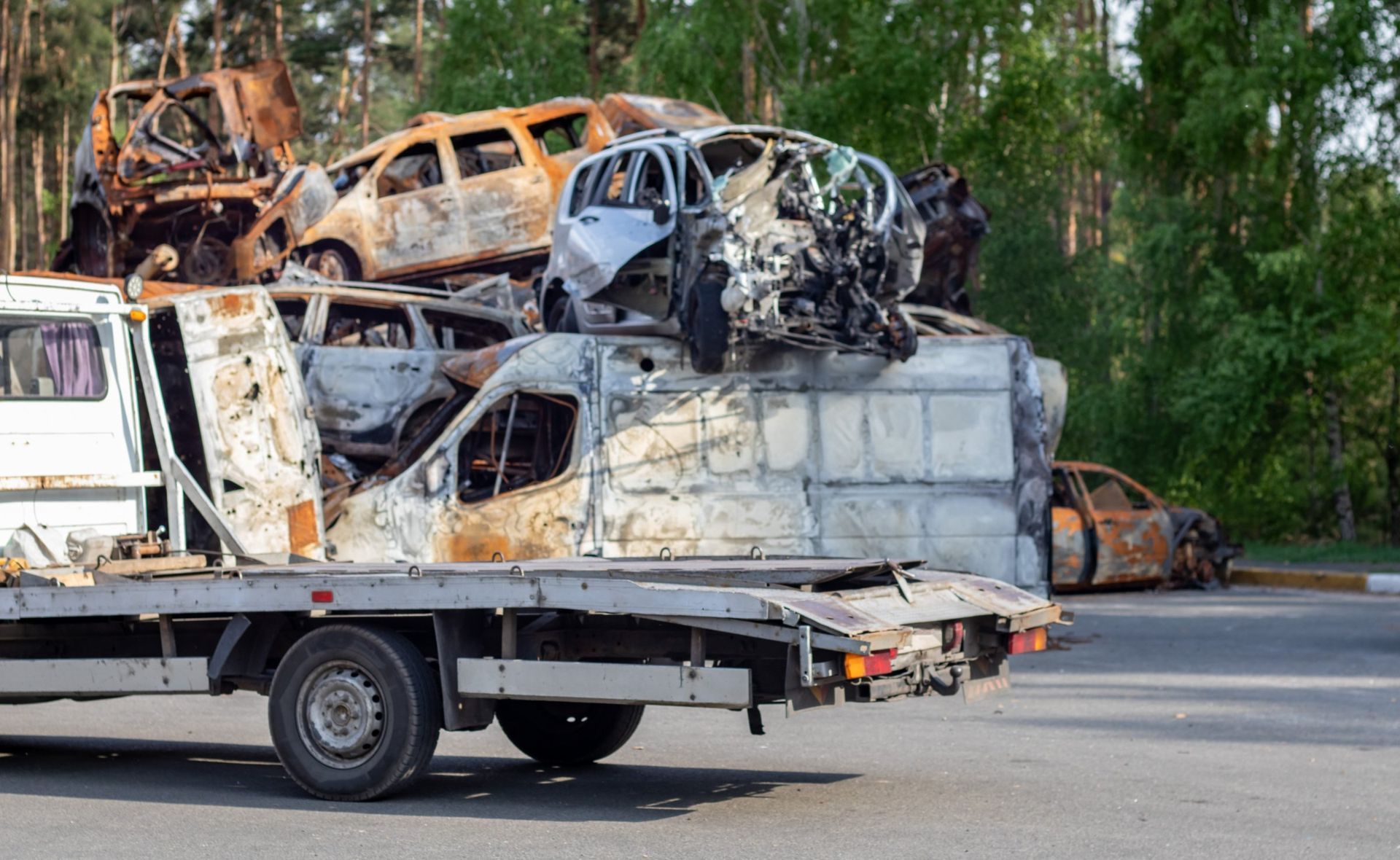A tow truck loaded with severely damaged and burned-out vehicles, likely wreckage from a disaster.