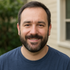 A man with a beard is wearing a blue shirt and smiling