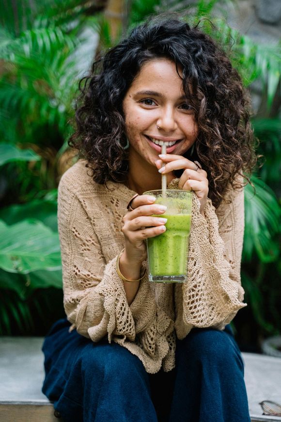 A woman is drinking a green smoothie through a straw.
