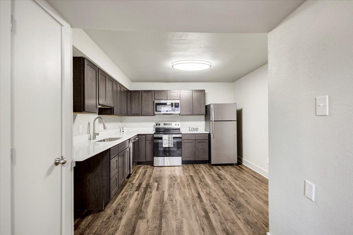 Kitchen with dark cabinets, stainless steel appliances, and wood-look flooring.