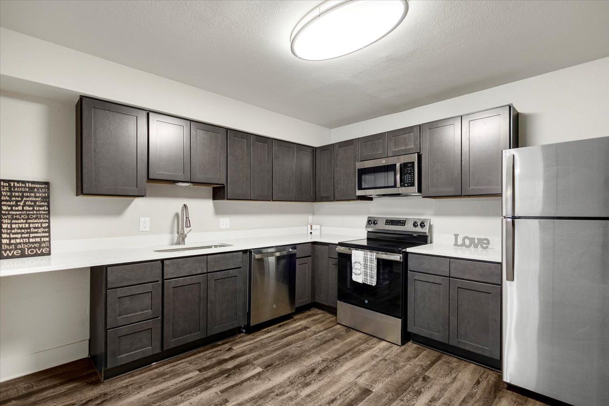 Modern kitchen with dark gray cabinets, stainless steel appliances, and wood-look flooring.