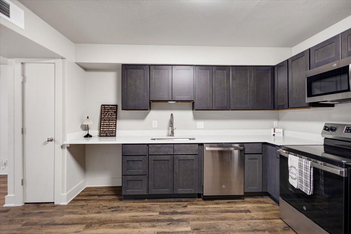 Modern kitchen with dark gray cabinets, stainless steel appliances, and a white countertop.