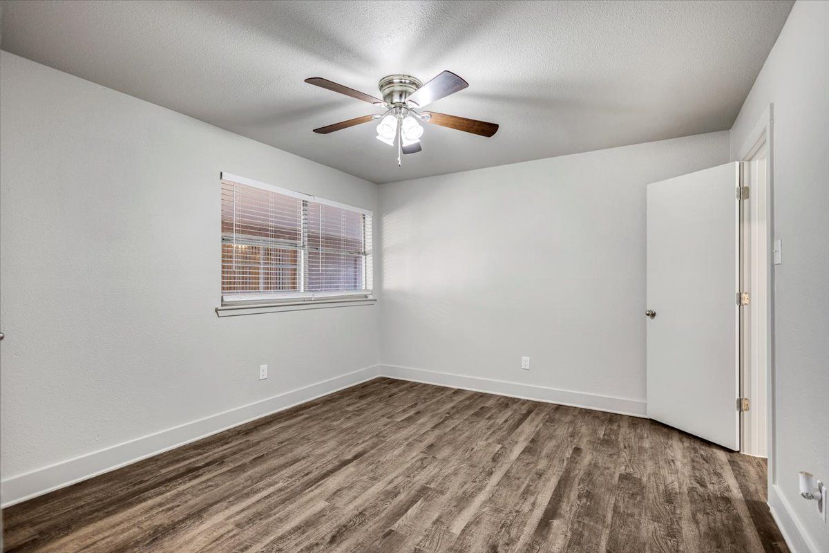 Empty bedroom with gray walls, wood-look flooring, window with blinds, and a ceiling fan.