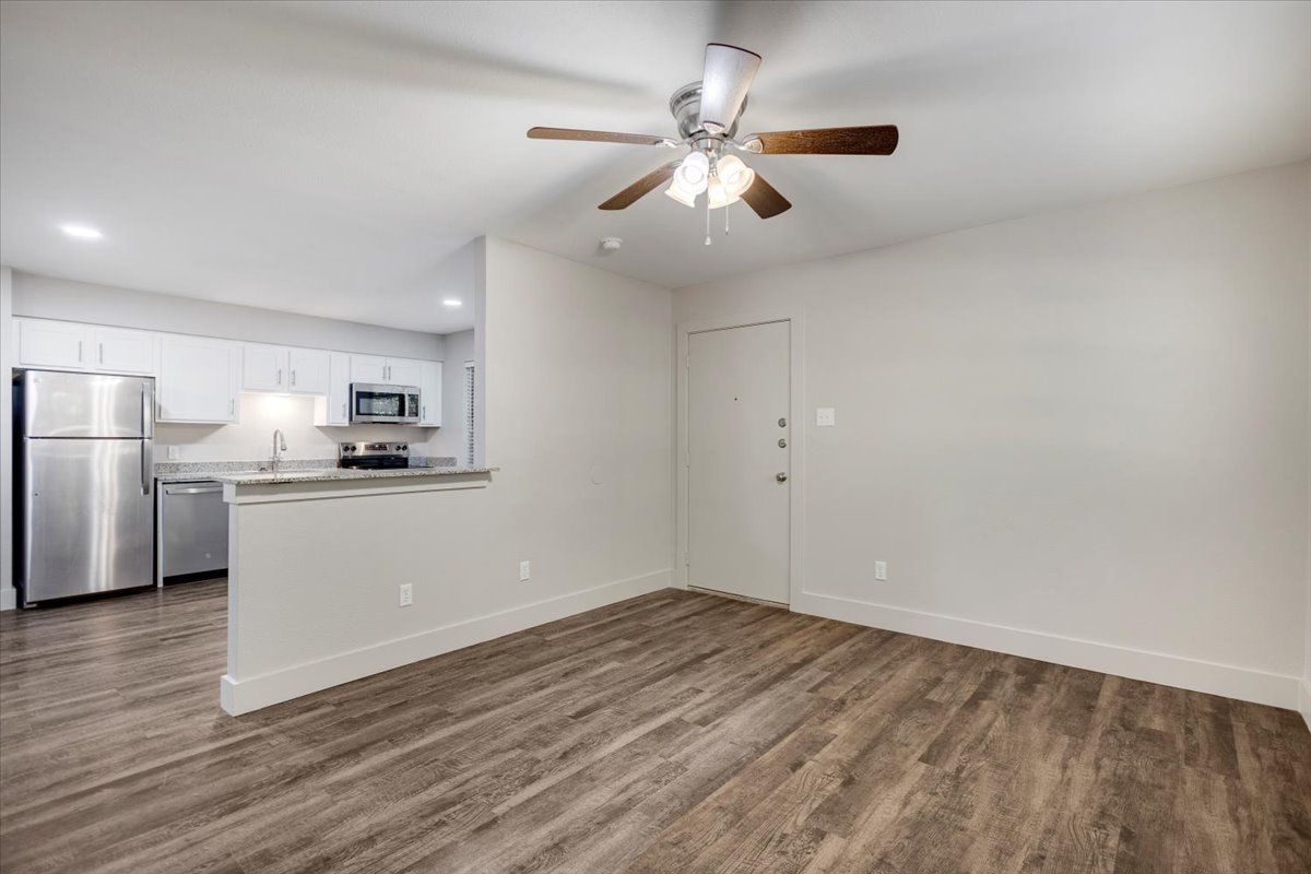 Open-concept living space with kitchen and wood-look flooring. White walls and cabinets, stainless steel appliances, ceiling fan.