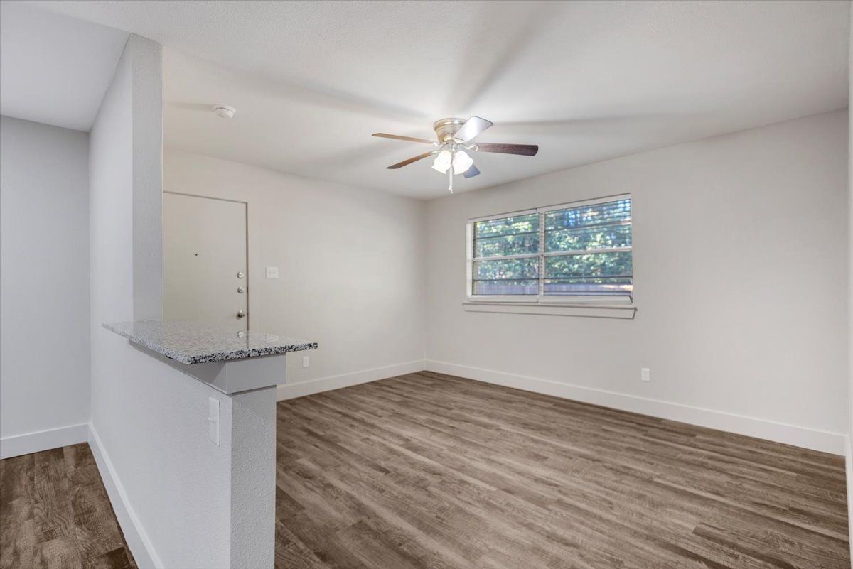 Empty room with gray walls, wood-look flooring, window, and countertop with a light fixture.