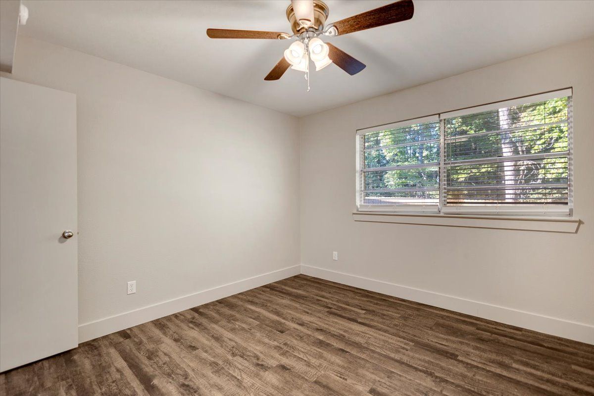Empty bedroom with wood-look flooring, white walls, a window, and a ceiling fan.