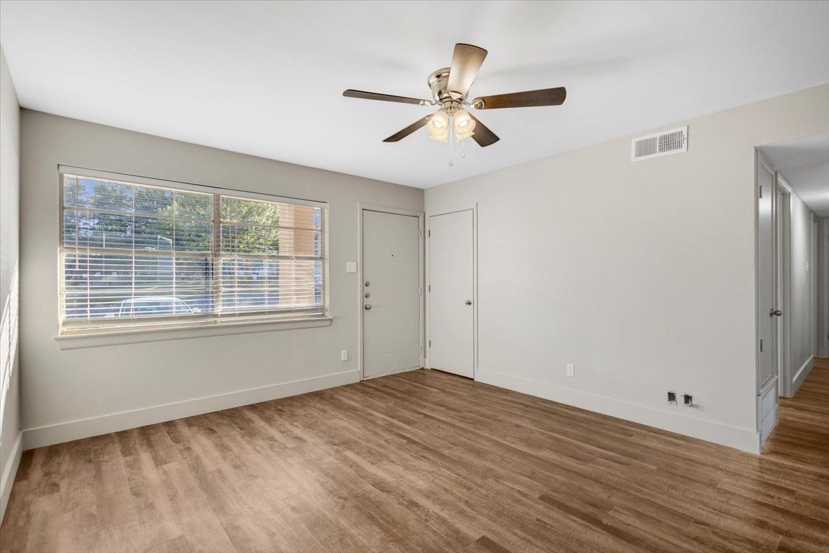 Empty room with wooden floors, neutral walls, window, door, and ceiling fan.