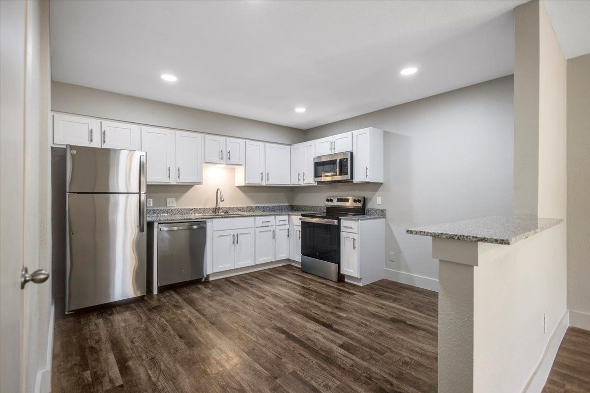 Modern kitchen with stainless steel appliances, white cabinets, granite countertops, and wood-look flooring.