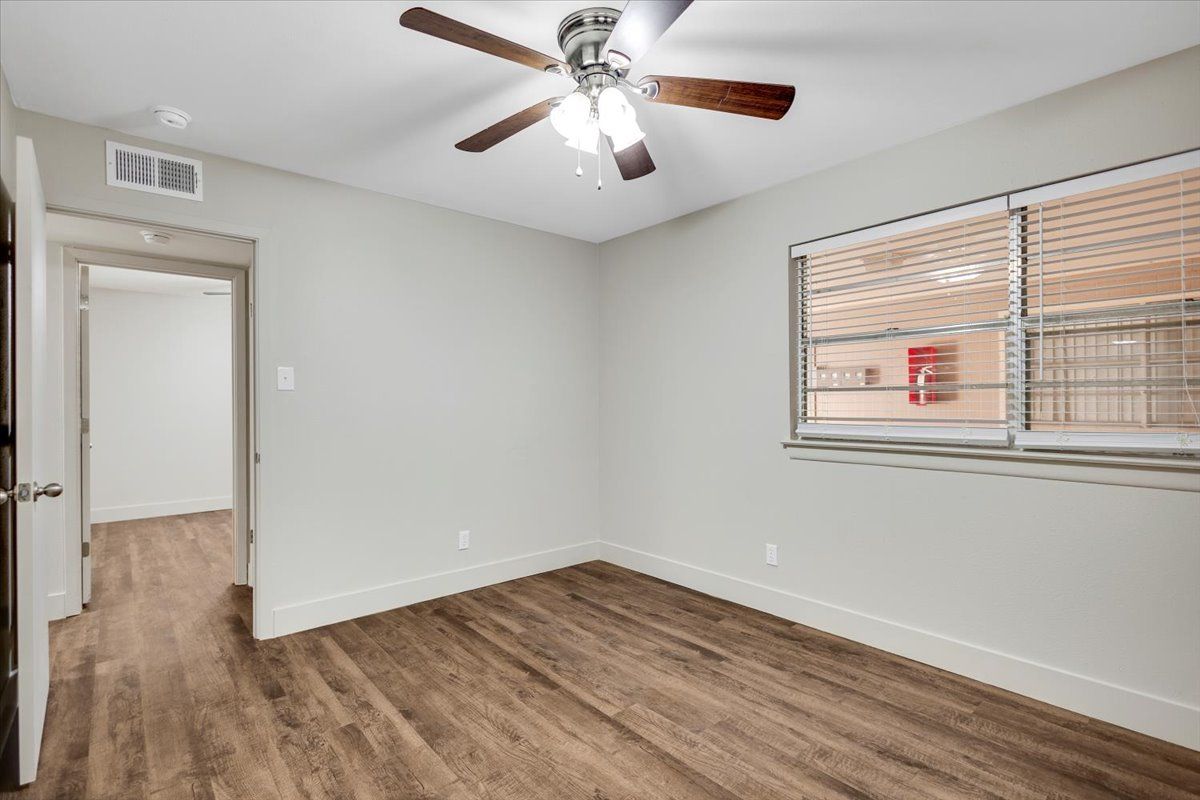 Empty bedroom with wood-look flooring, light gray walls, window, and ceiling fan.