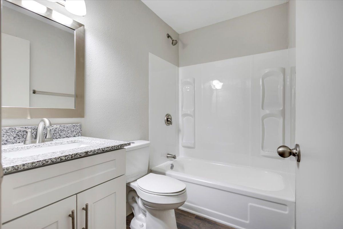Bathroom with white tub, toilet, vanity, and light gray walls.