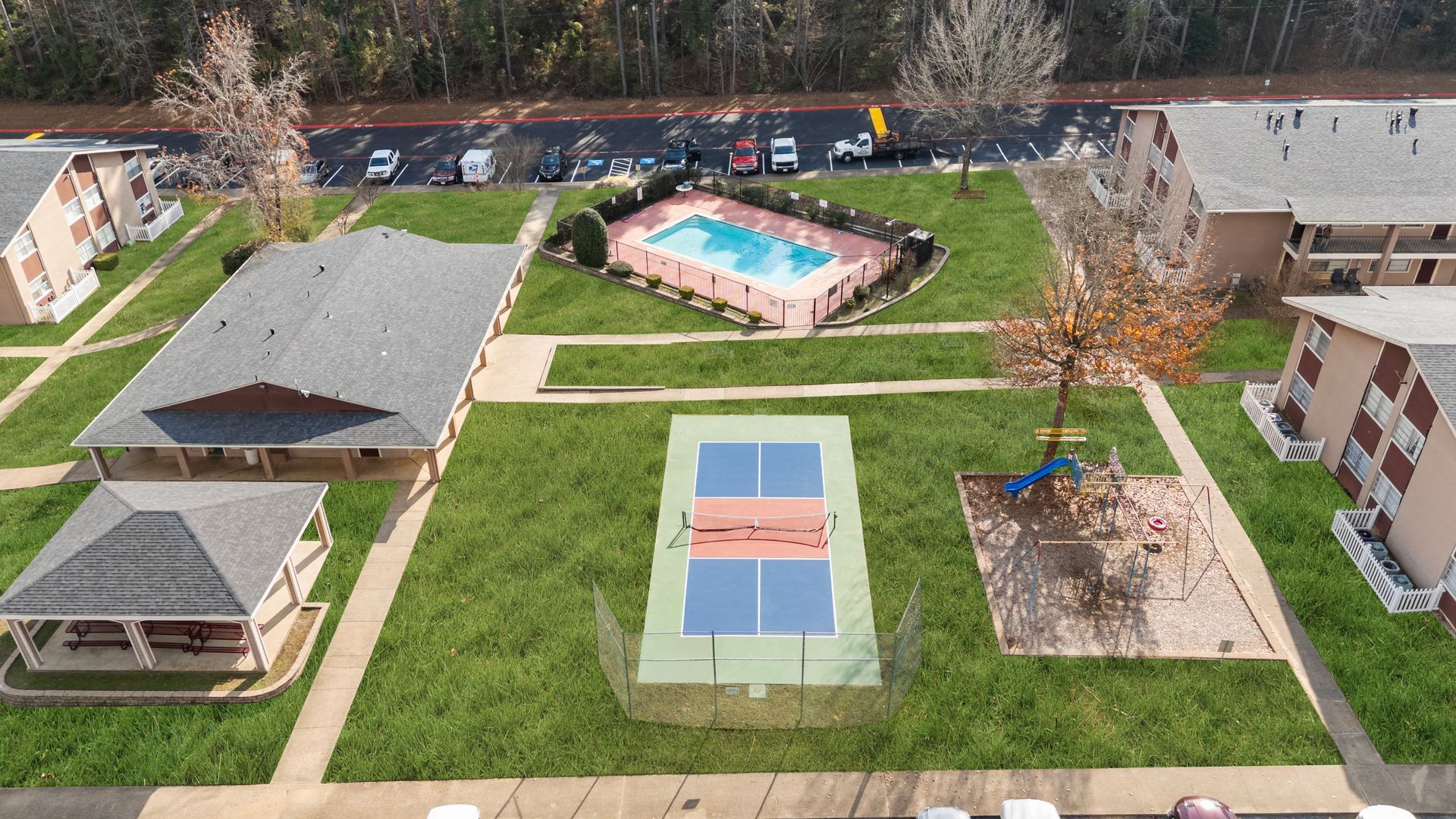 Aerial view of apartment complex with a pool, tennis court, and playground.