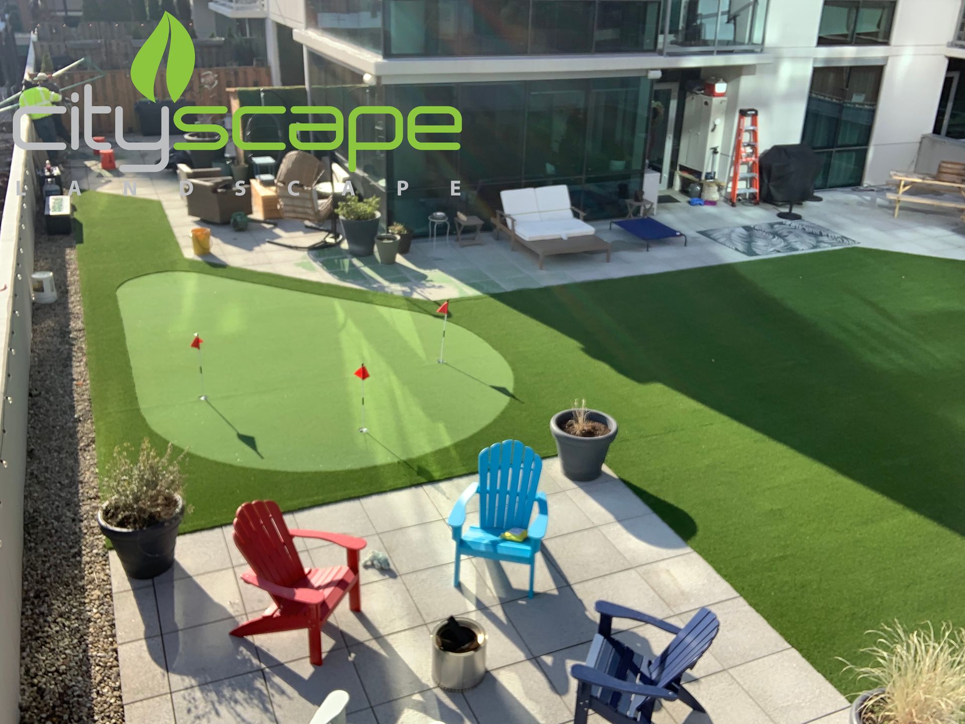A rooftop patio with artificial turf, a putting green, and colorful Adirondack chairs.