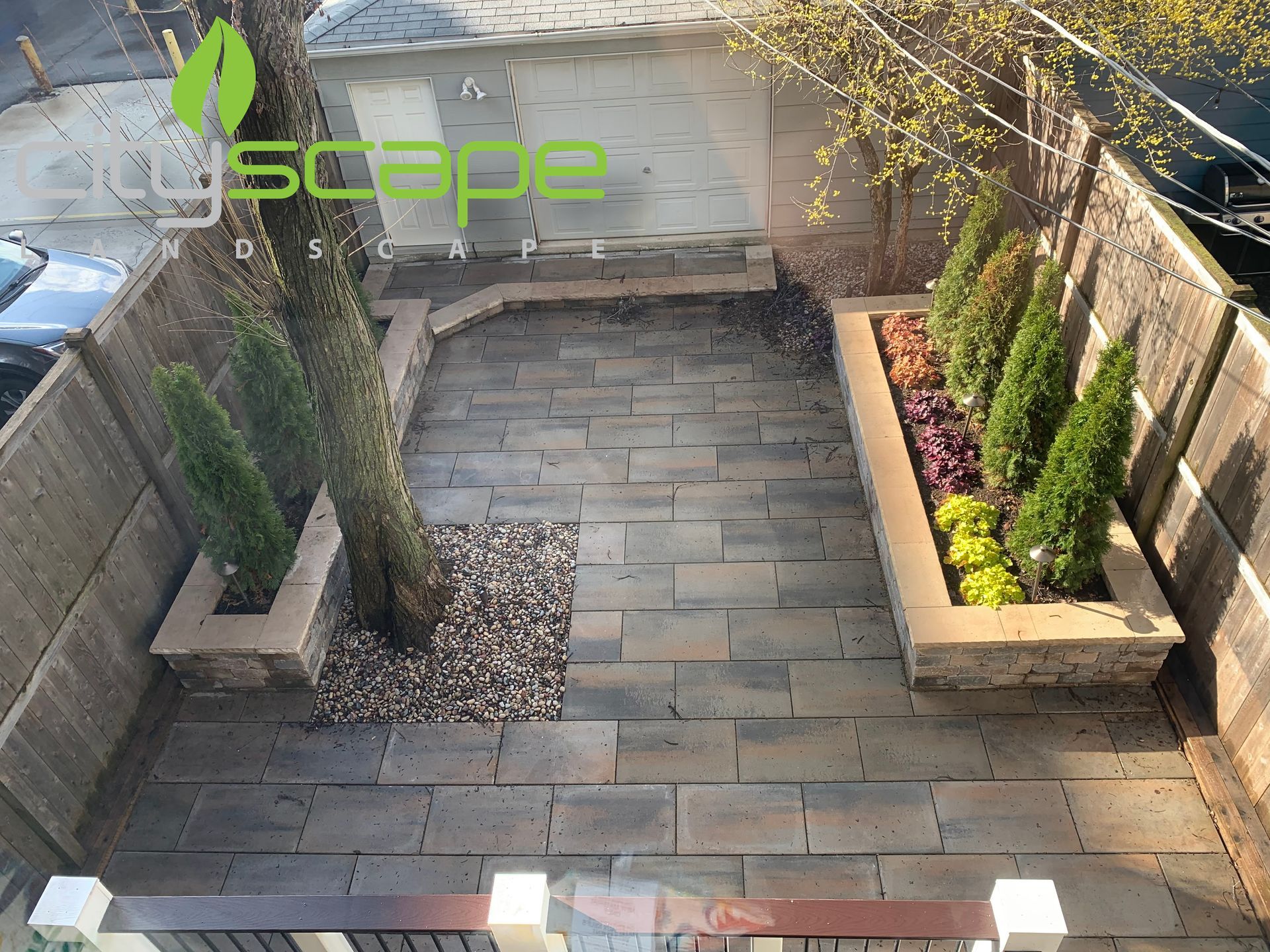 Small, paved backyard with planters, trees, and a wooden fence.