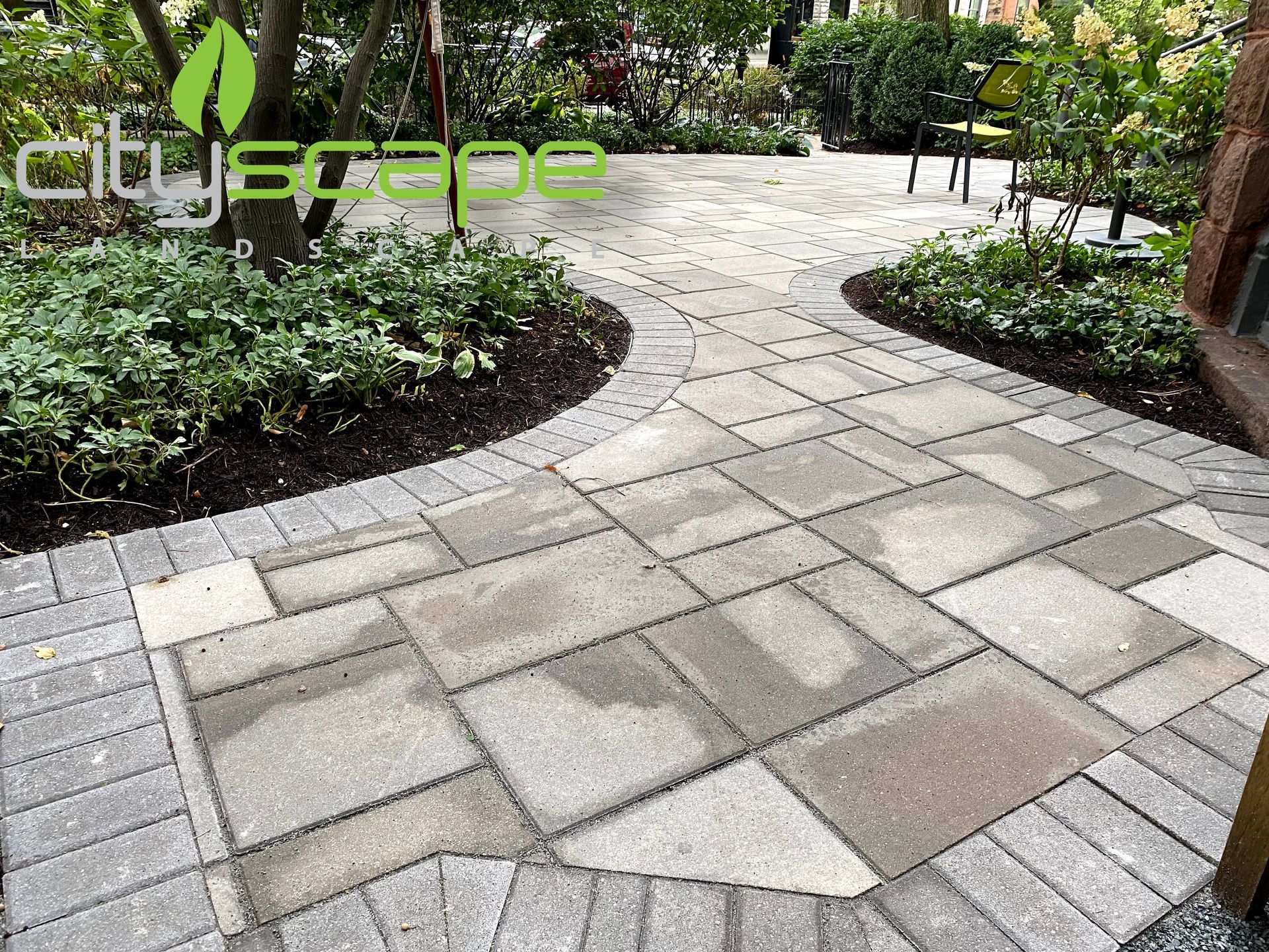 Brick patio with varied stone pattern, surrounded by greenery and mulch beds; cityscape logo in the corner.