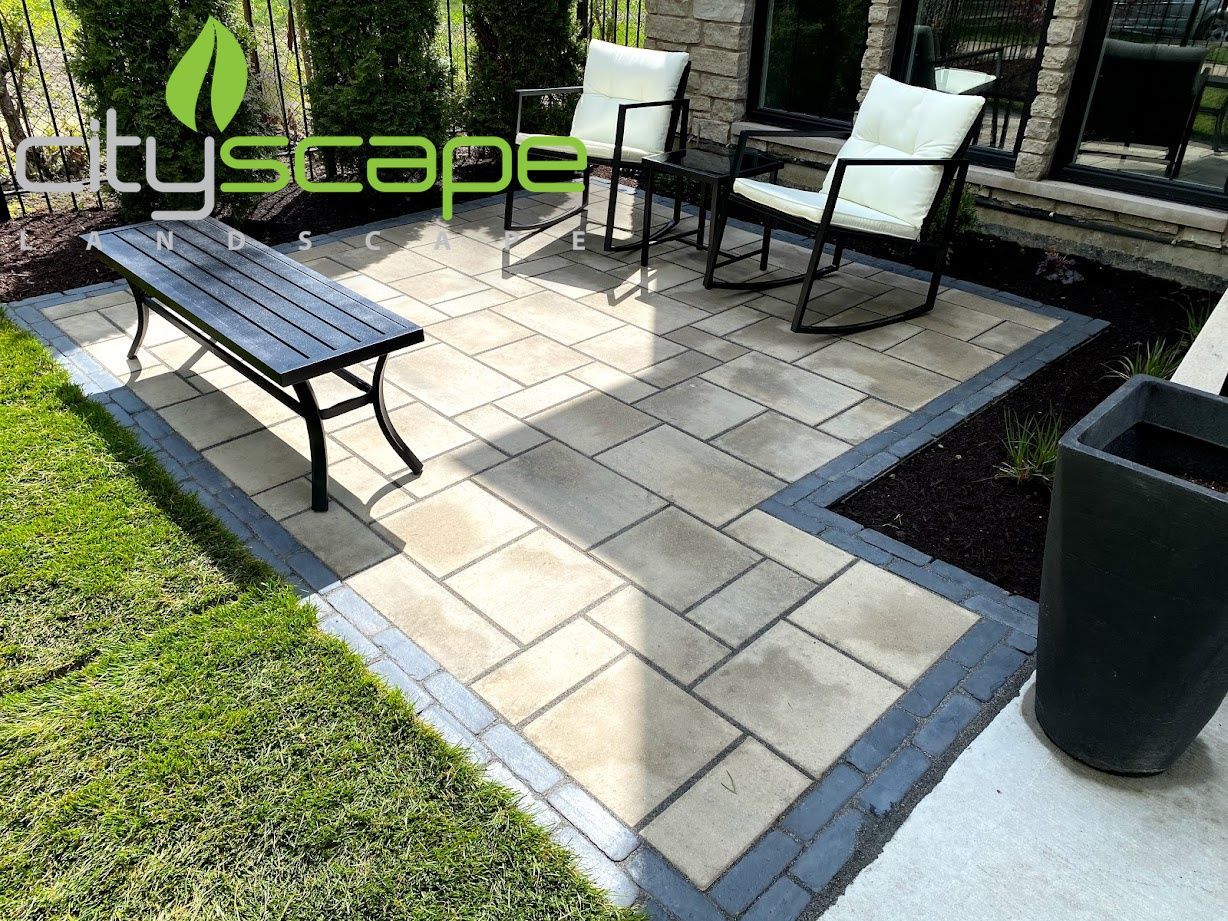 Backyard patio with covered furniture, gray building, wooden stairs, and stone patio.
