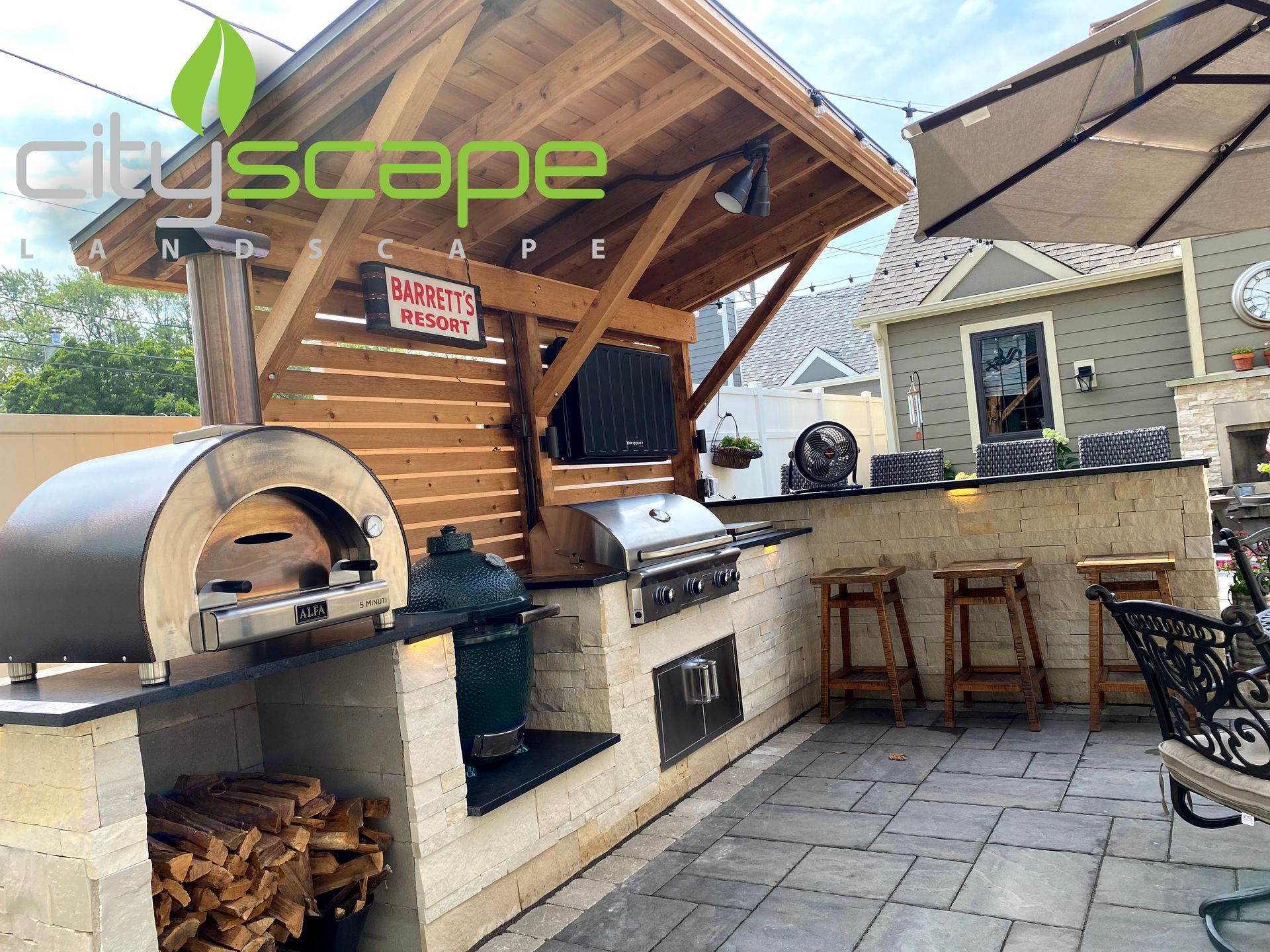 Outdoor kitchen with pizza oven, grill, Big Green Egg, bar seating, and wooden overhead structure.