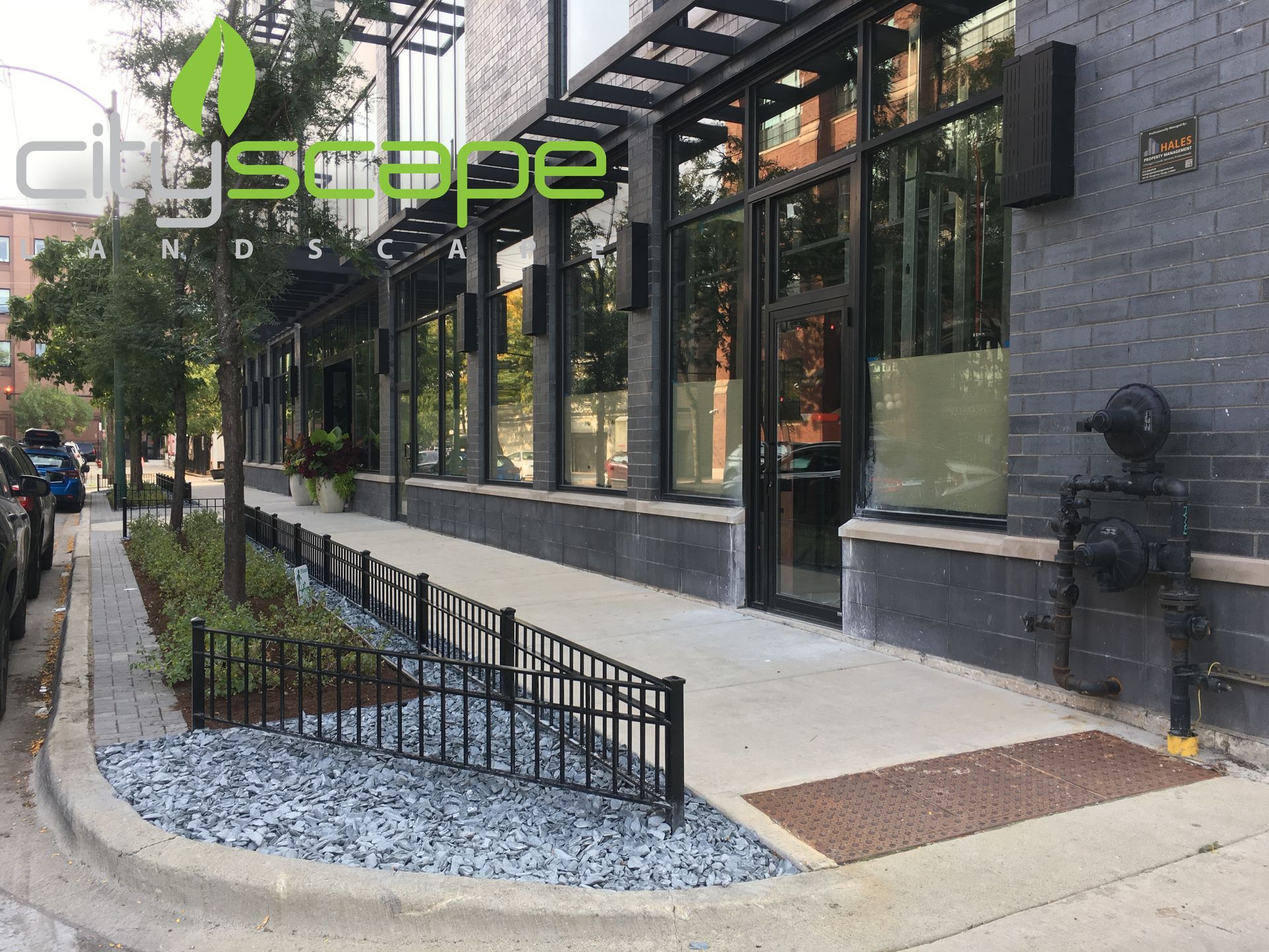 Exterior of a building with a ramp, sidewalk, and landscaping. Dark gray brick wall, black metal railings.