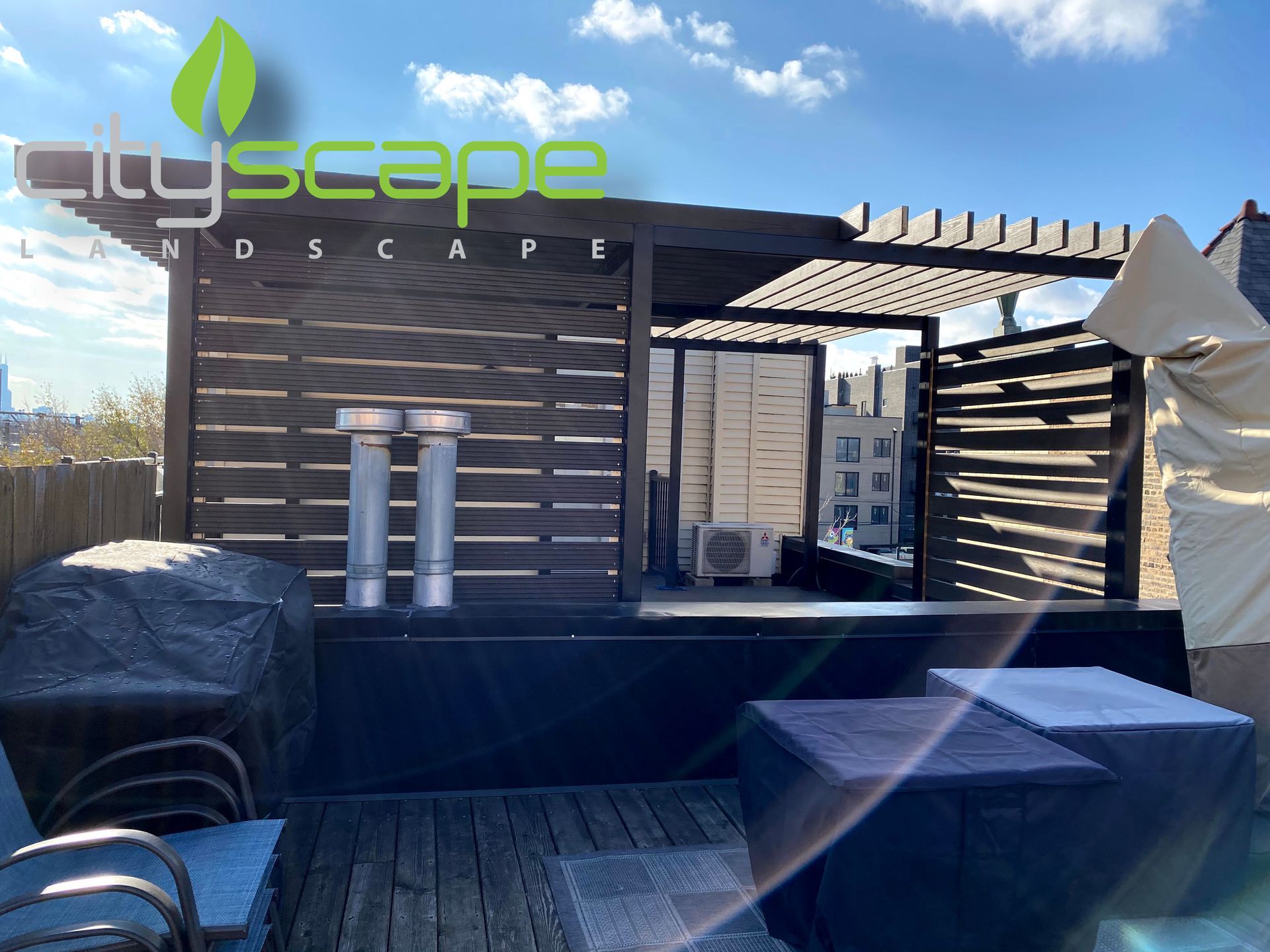 Rooftop deck with black wooden structures, pergola, and covered furniture; city view in background.