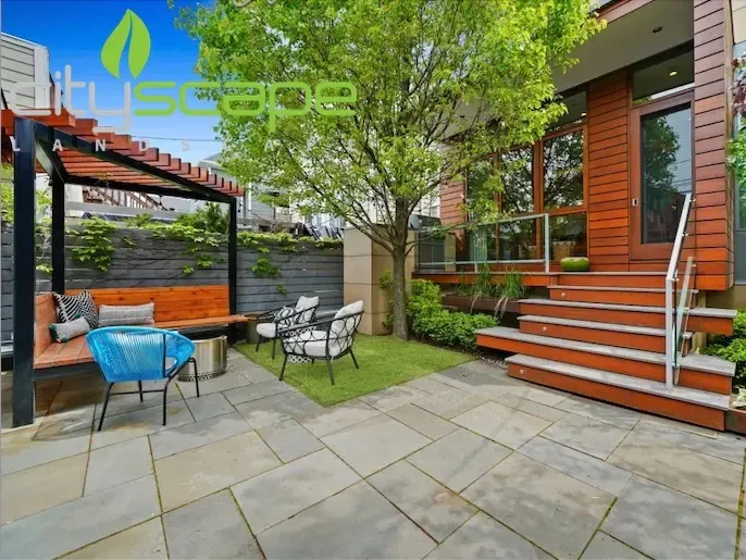 Backyard patio with bar, hot tub, and greenery. Gray pavers and brick exterior.