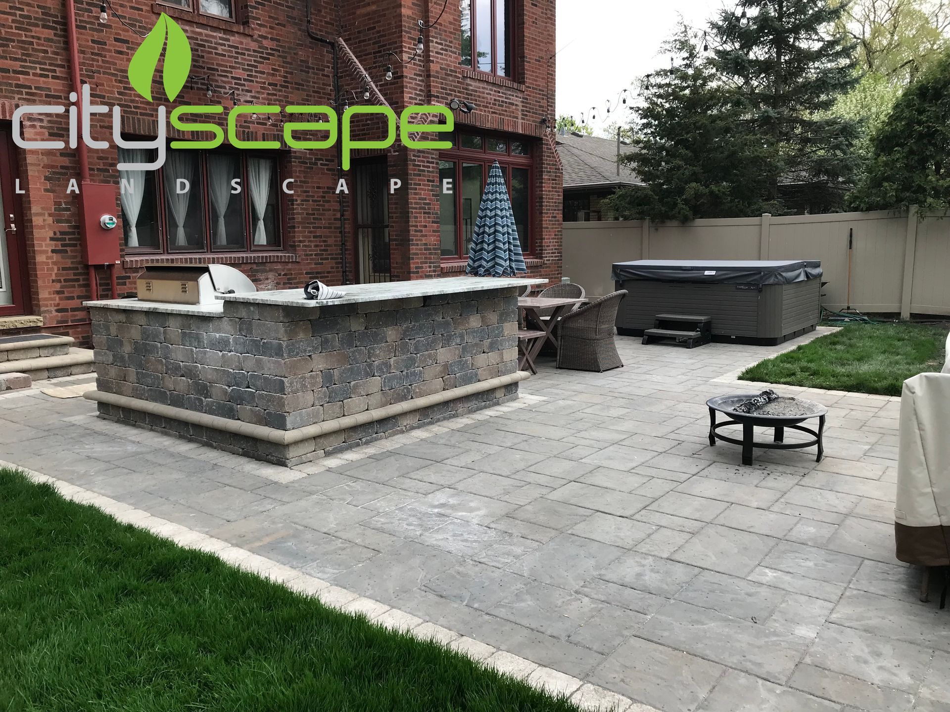 Backyard patio with bar, hot tub, and green lawn. Brick house in the background.