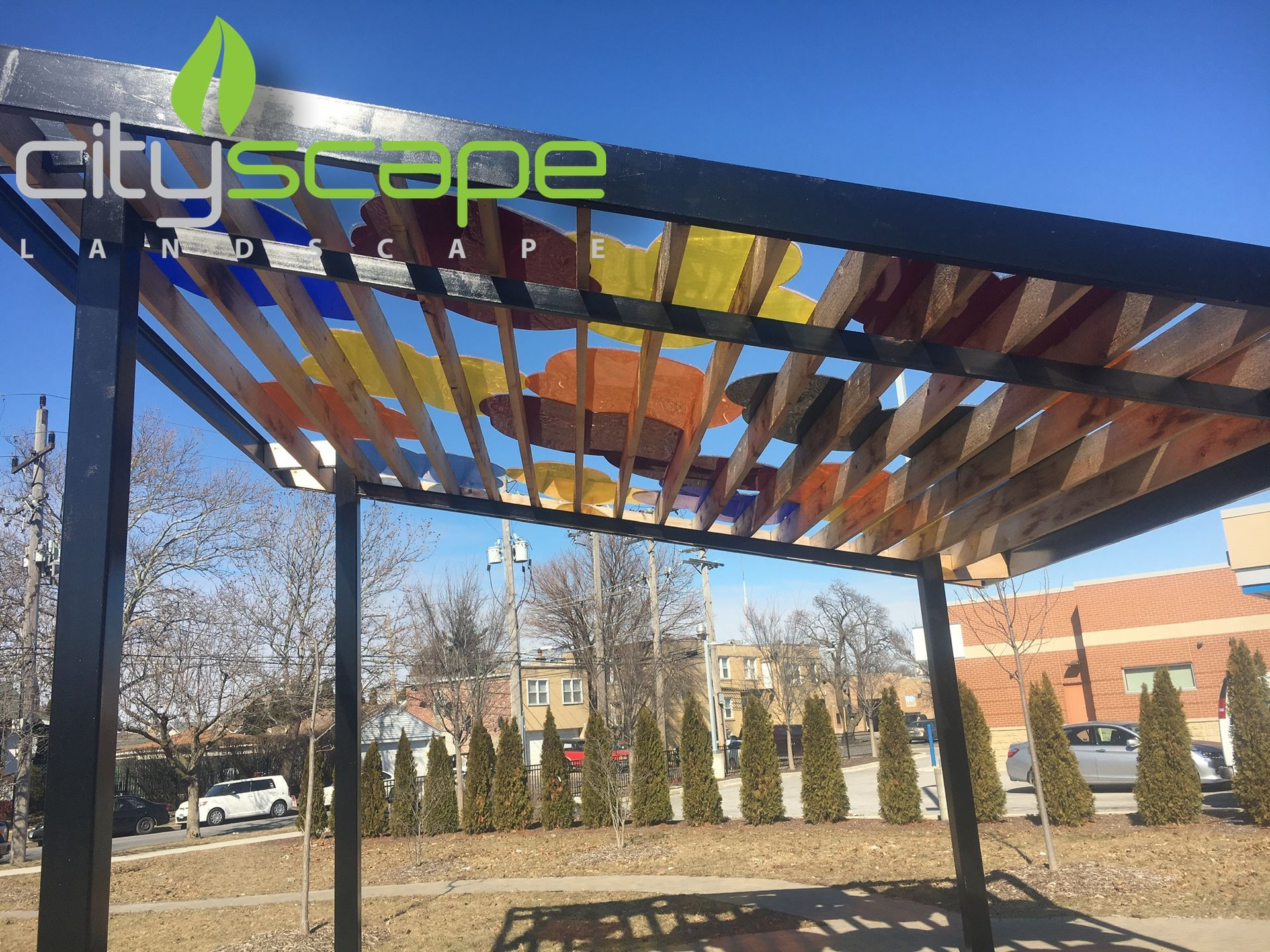 A modern pergola with colorful, transparent panels, under a bright blue sky.