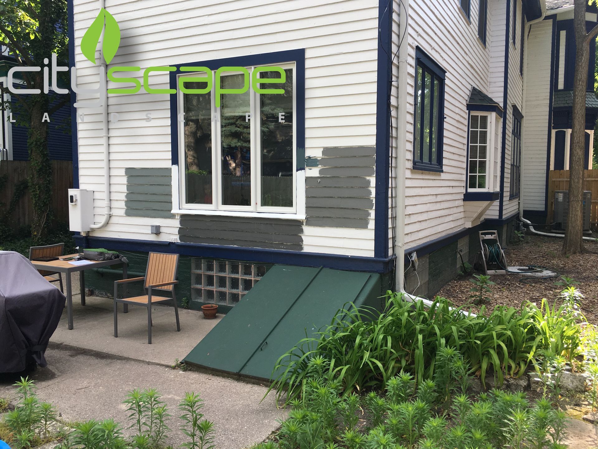 Back of a house with peeling paint, a green basement door, and outdoor furniture.