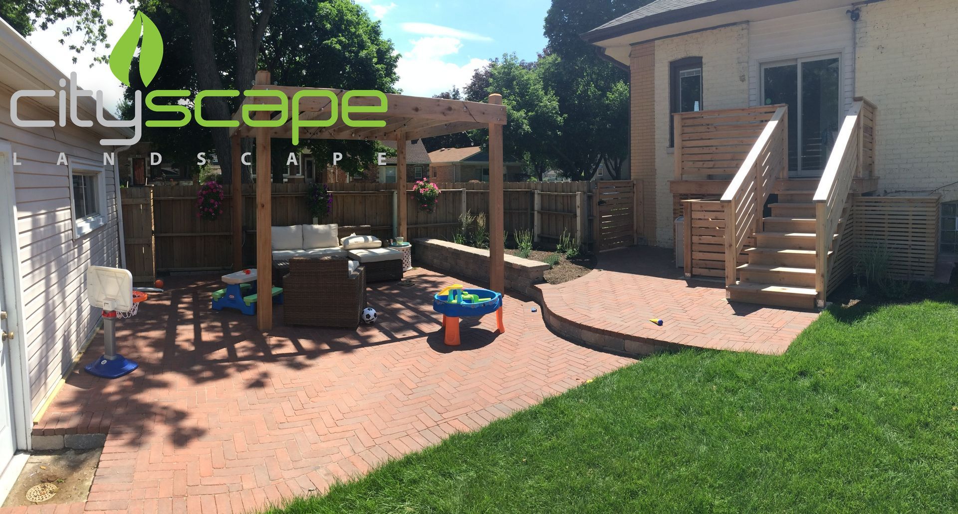 Backyard patio with brick pavers, wooden pergola, steps, and play area.