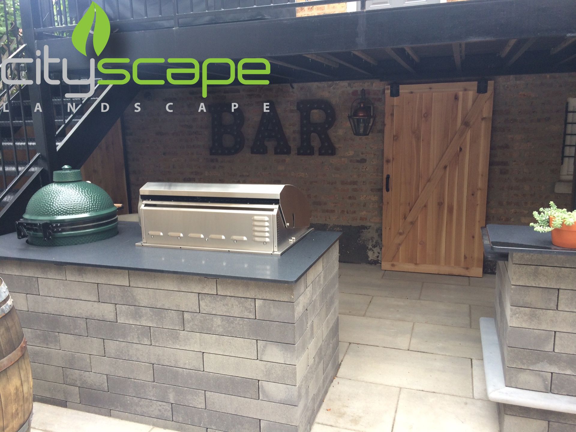 Outdoor kitchen with grill, Big Green Egg, and bar next to a sliding wooden door.