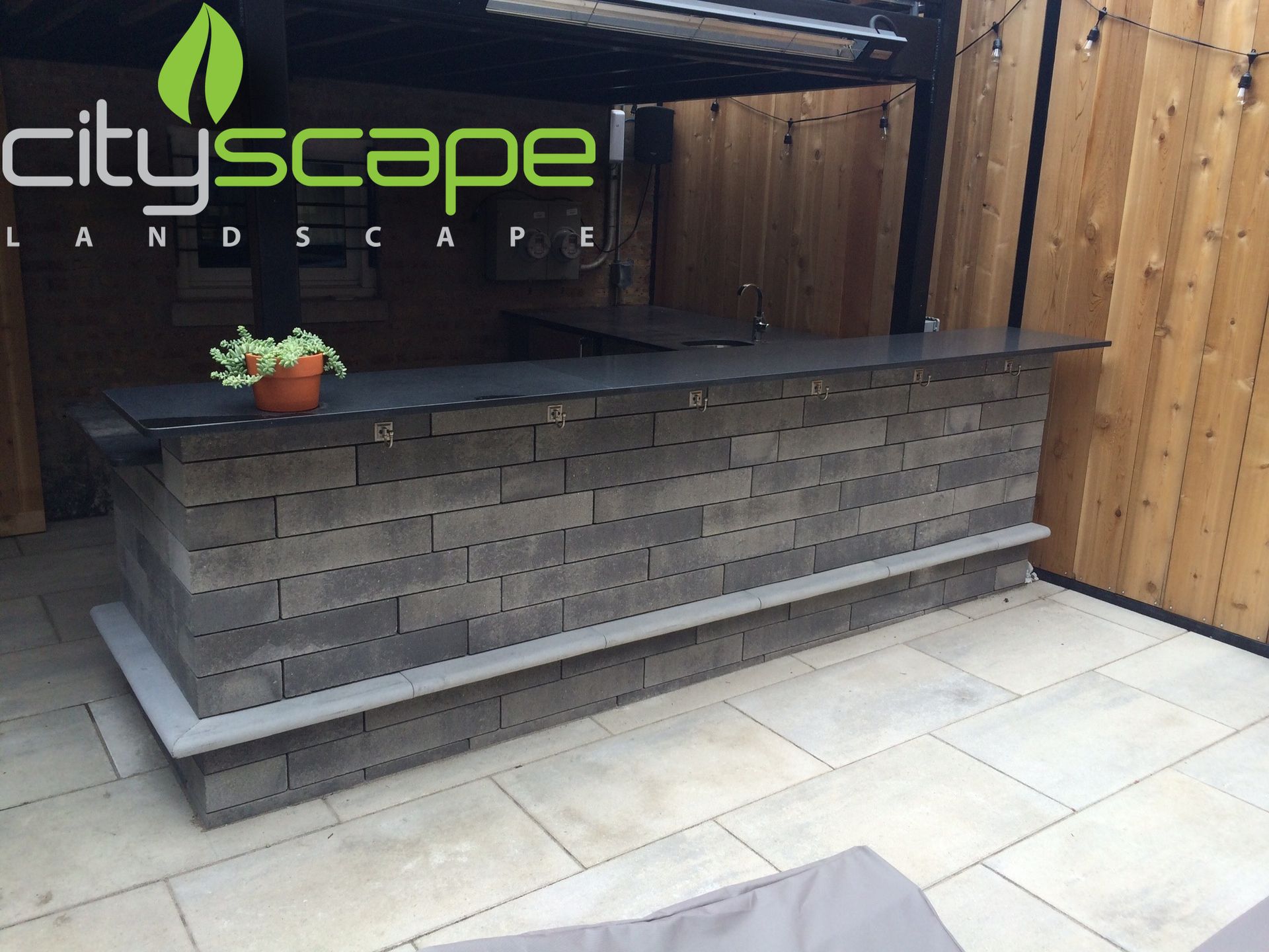 Outdoor bar constructed of gray blocks with a dark countertop and a small plant, in a patio setting.